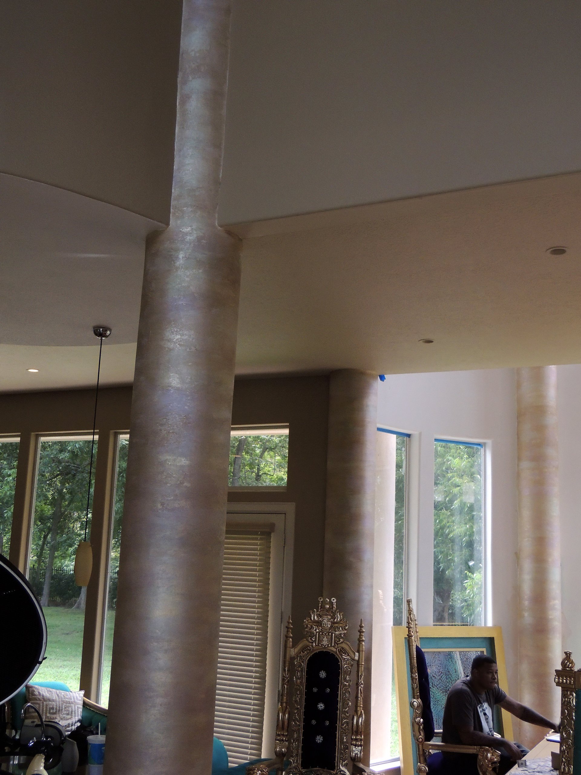 Travertine faux plaster finish on tall round columns in a grand residential great-room with warm taupe tones.