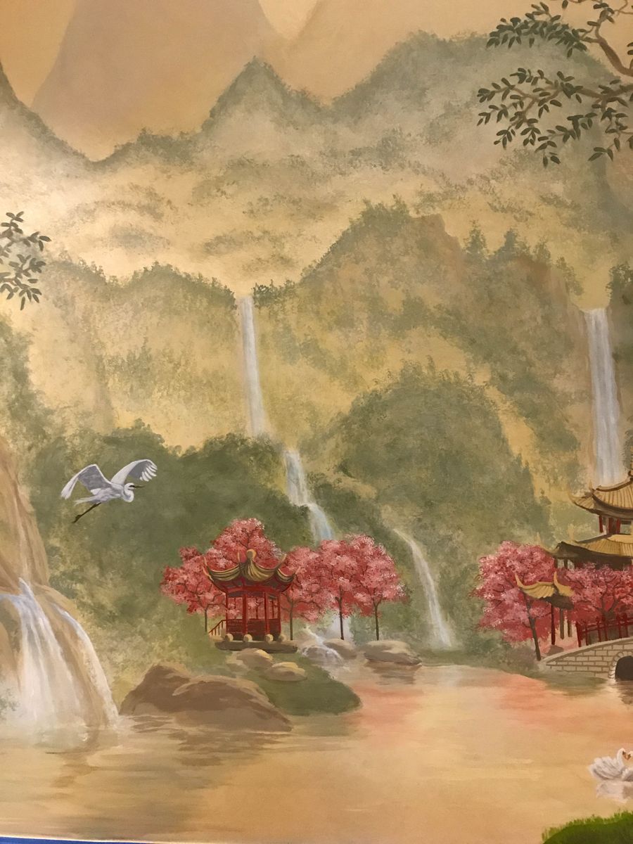 Hand-painted Chinese landscape mural with red pagodas, cherry blossoms, misty mountains, and cascading waterfalls on warm gold wall