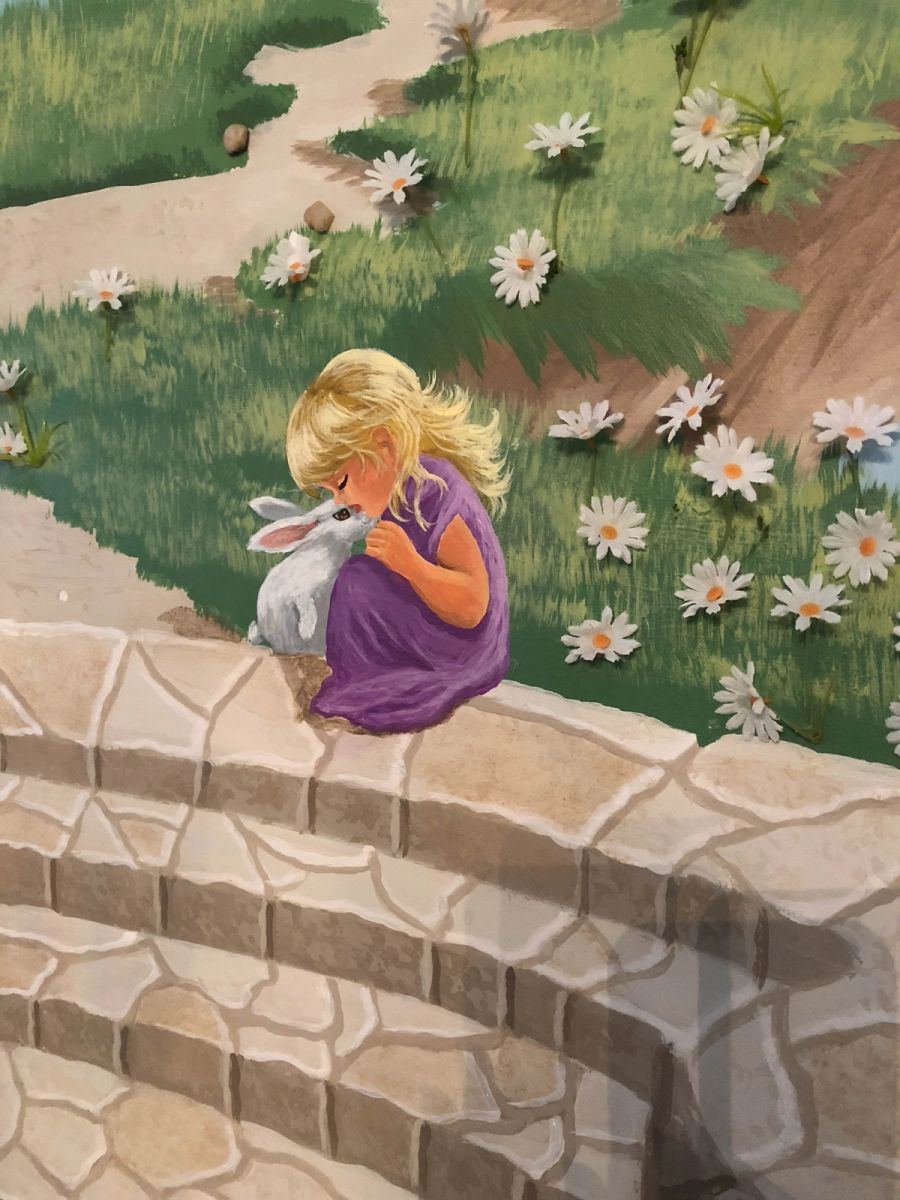 Hand-painted children's mural of girl with bunny on stone wall surrounded by daisies, figurative narrative wall art