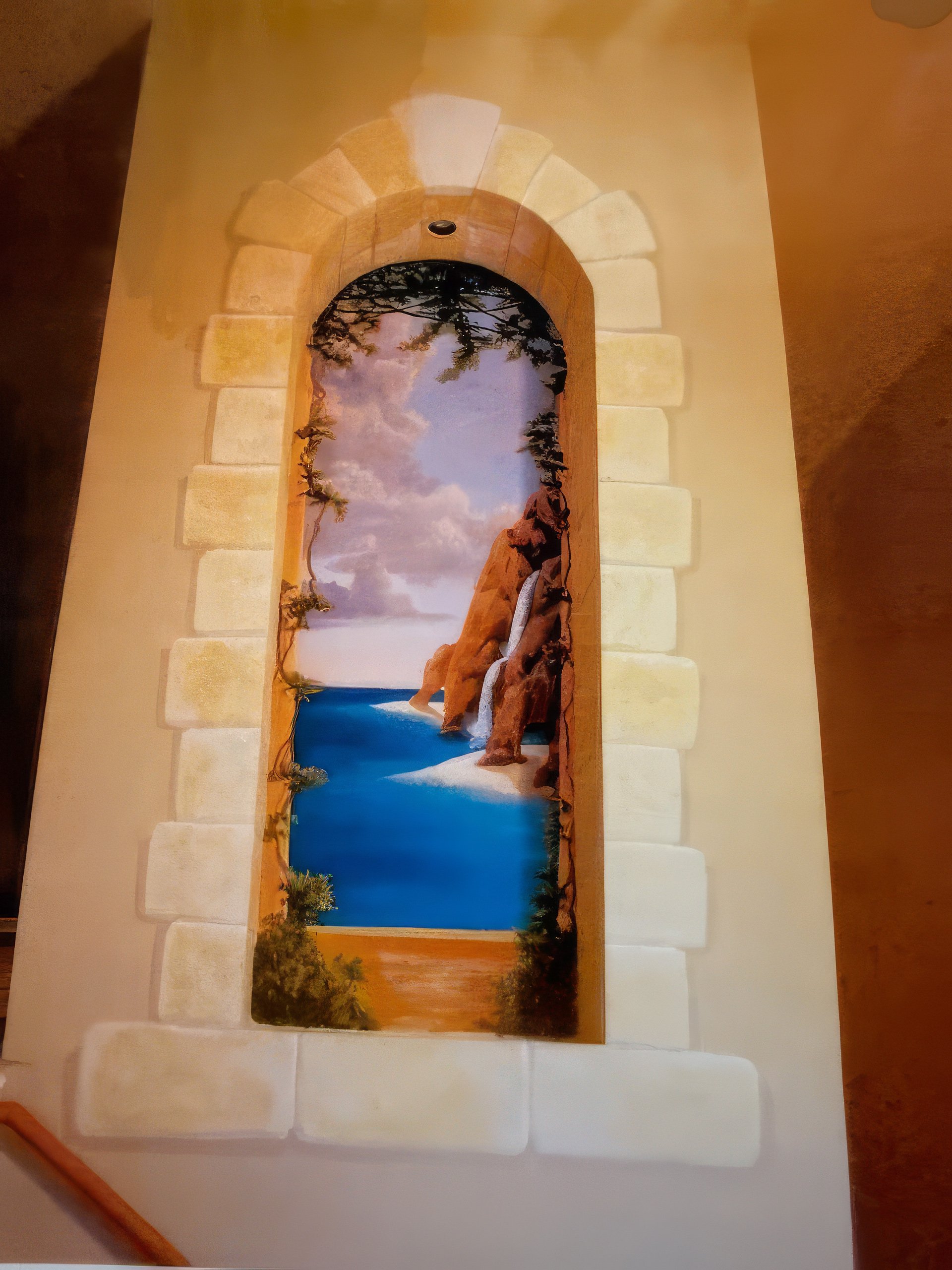 Trompe l'oeil faux stone arch mural in hallway depicting coastal waterfall scene, residential decorative wall art