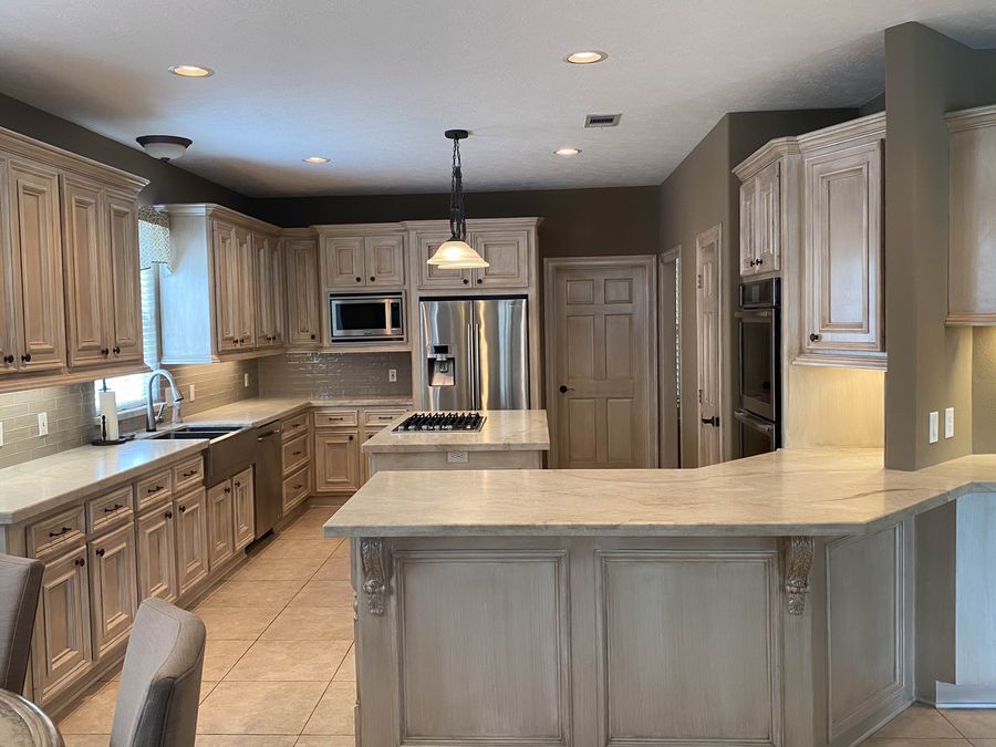 Antiqued glazed kitchen cabinets with brown umber glaze on cream base, contrasting gray-silver glazed island with corbel brackets.