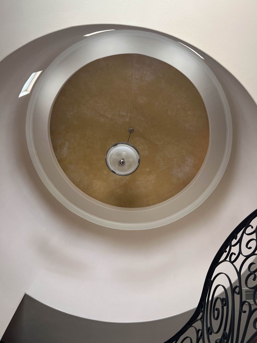 Gold Venetian plaster rotunda dome ceiling in luxury foyer with concentric white molding rings and pendant light