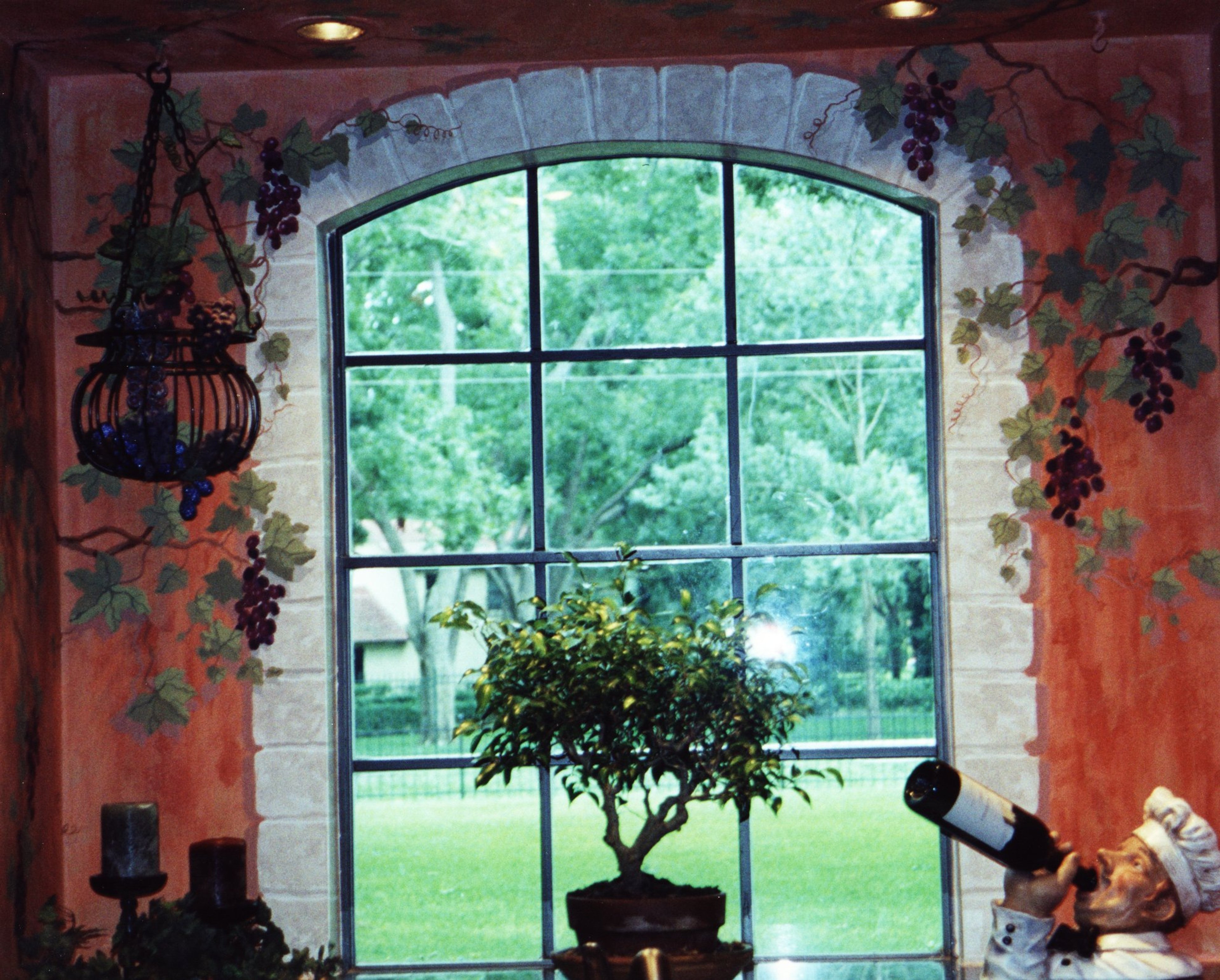 Tuscan faux fresco kitchen walls with hand-painted trompe l'oeil grapevine mural framing arched window, Houston.