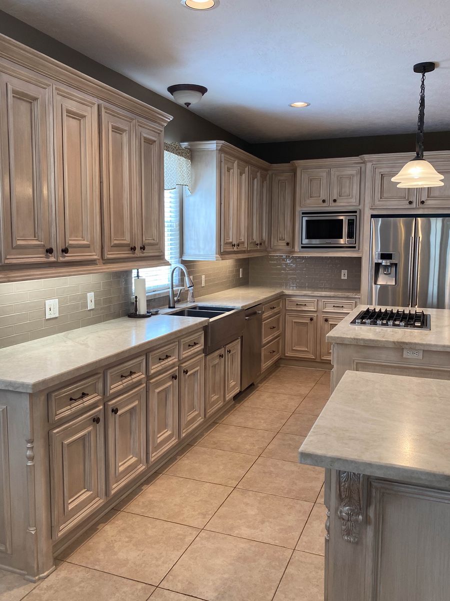 Antiqued brown-glazed kitchen cabinets with warm beige base, raised-panel doors, marble countertops, and subway tile backsplash.