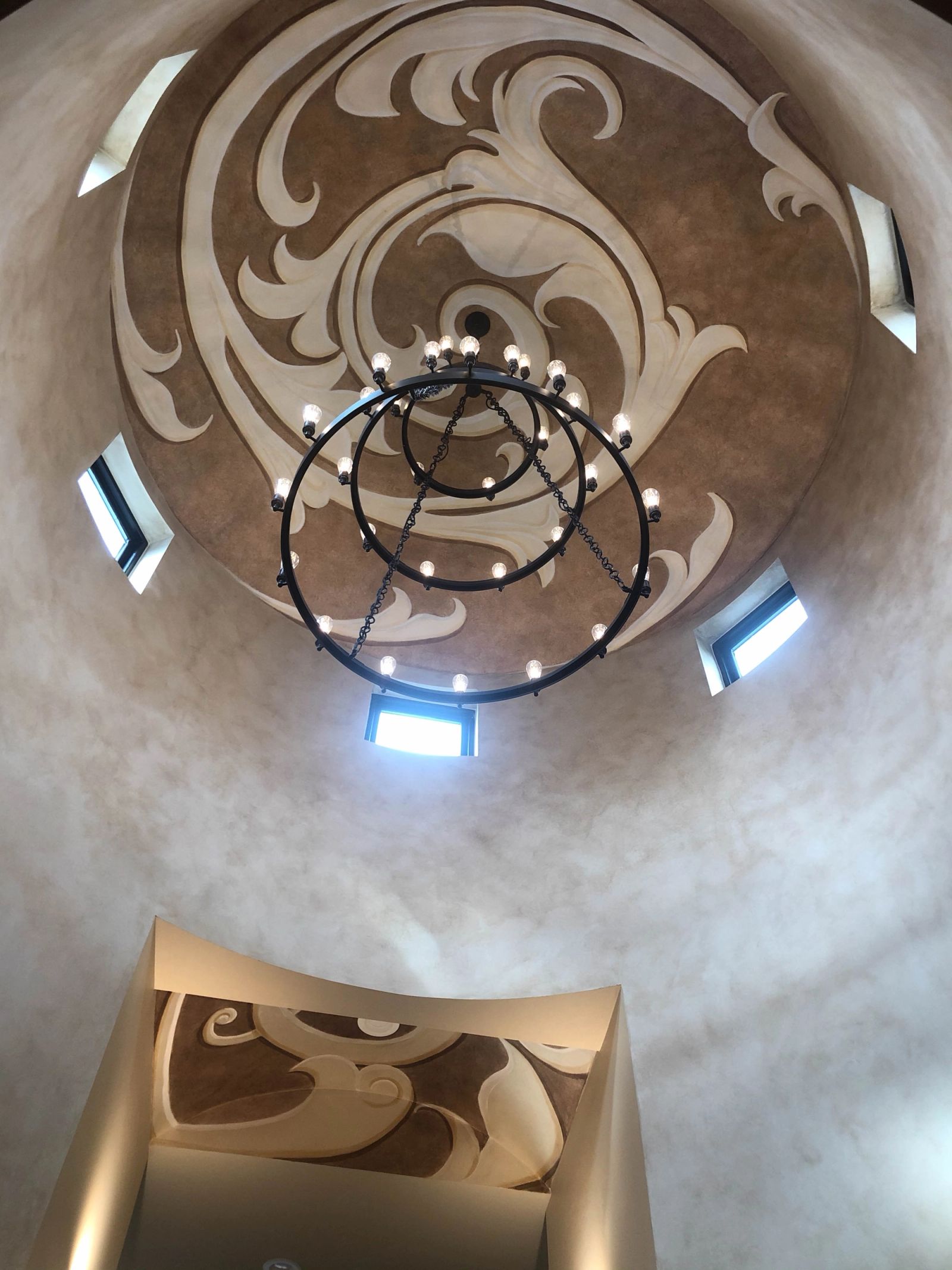 Hand-painted acanthus scrollwork dome with Venetian plaster drum walls and iron chandelier in grand foyer rotunda.