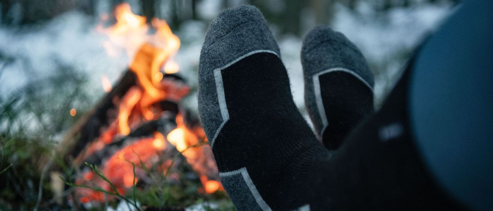 två fötter i varma strumpor som värmer sig vid en brasa i skogen