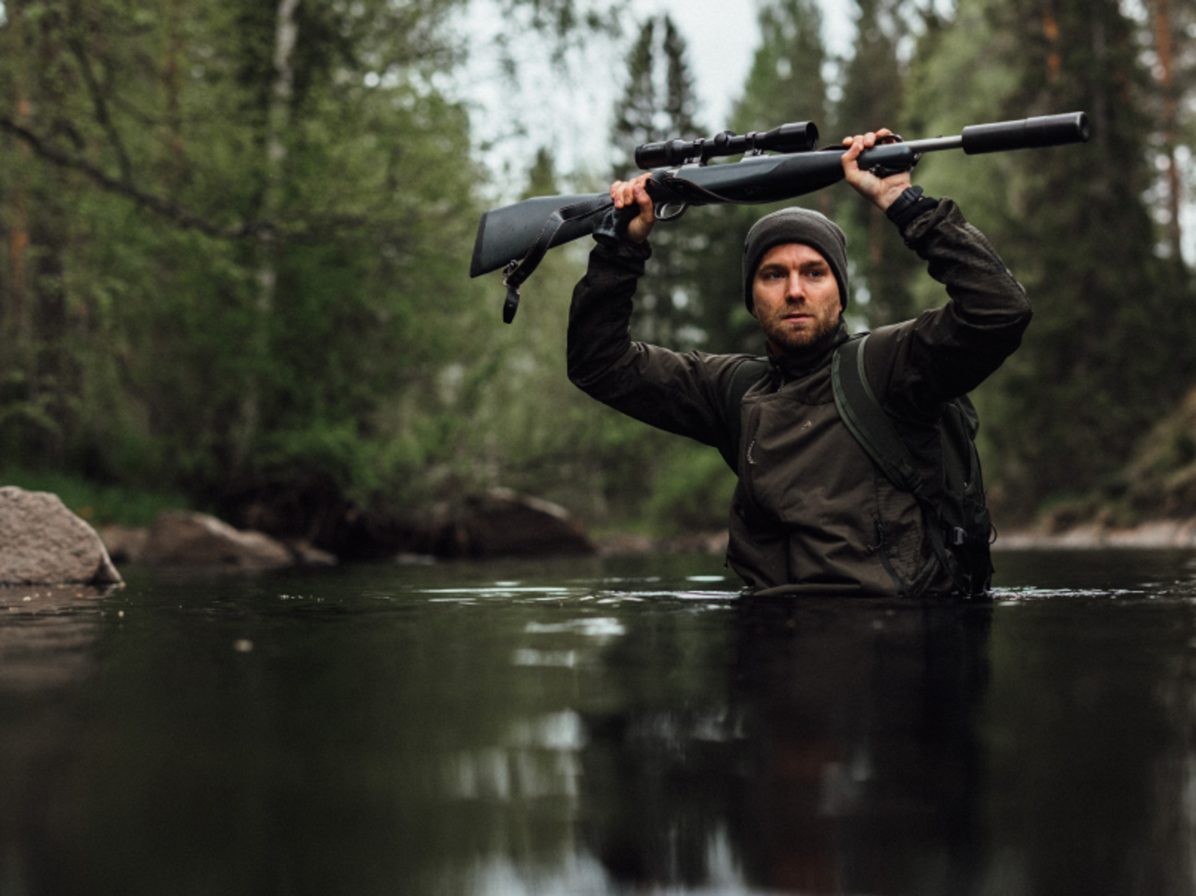 en jägare som vadar över en å och håller geväret över huvudet