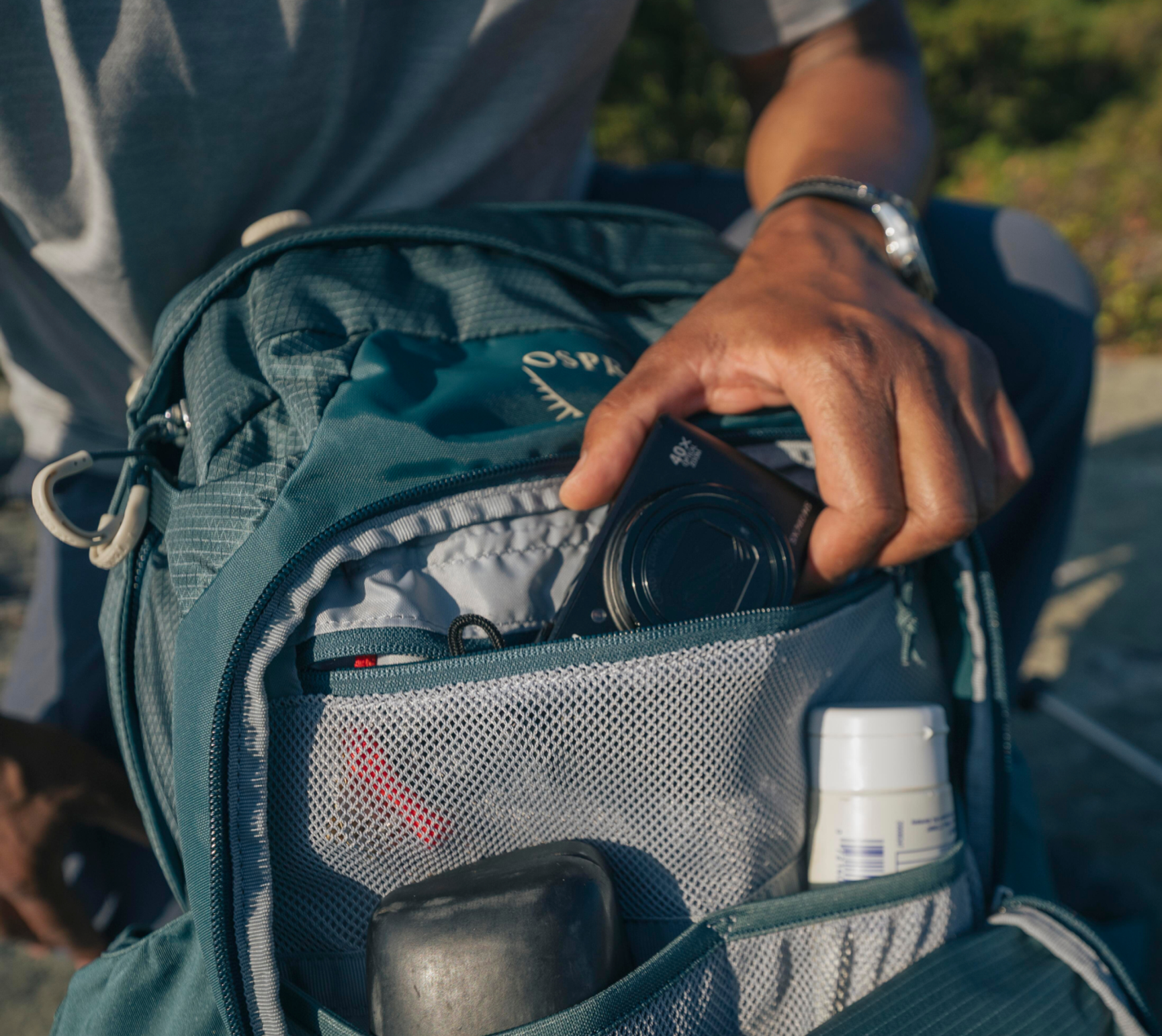 en hand som tar upp en kamera ur en outdoorryggsäck
