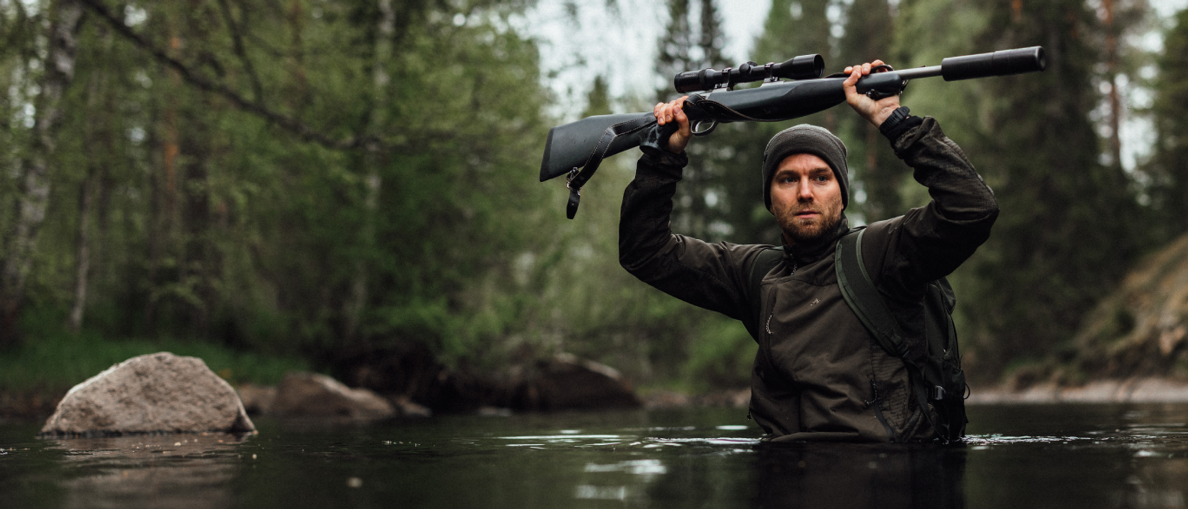 en jägare som vadar över en å och håller geväret över huvudet