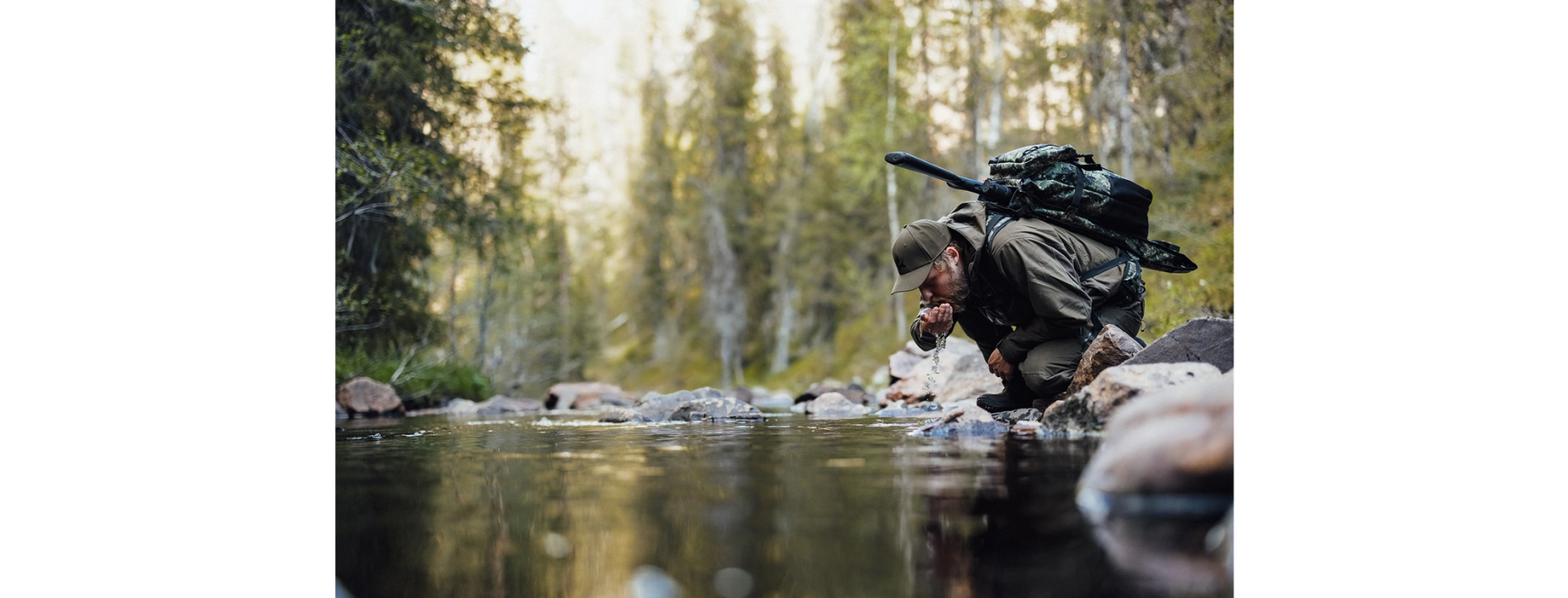 man med vapenryggsäck som dricker ur en skogsbäck