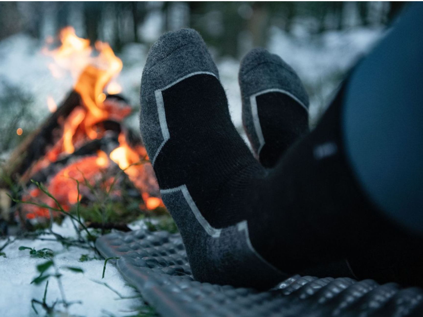 två fötter i varma strumpor som värmer sig vid en brasa i skogen