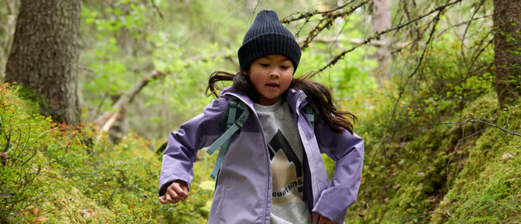 barn i lila jacka som springer på en skogsstig