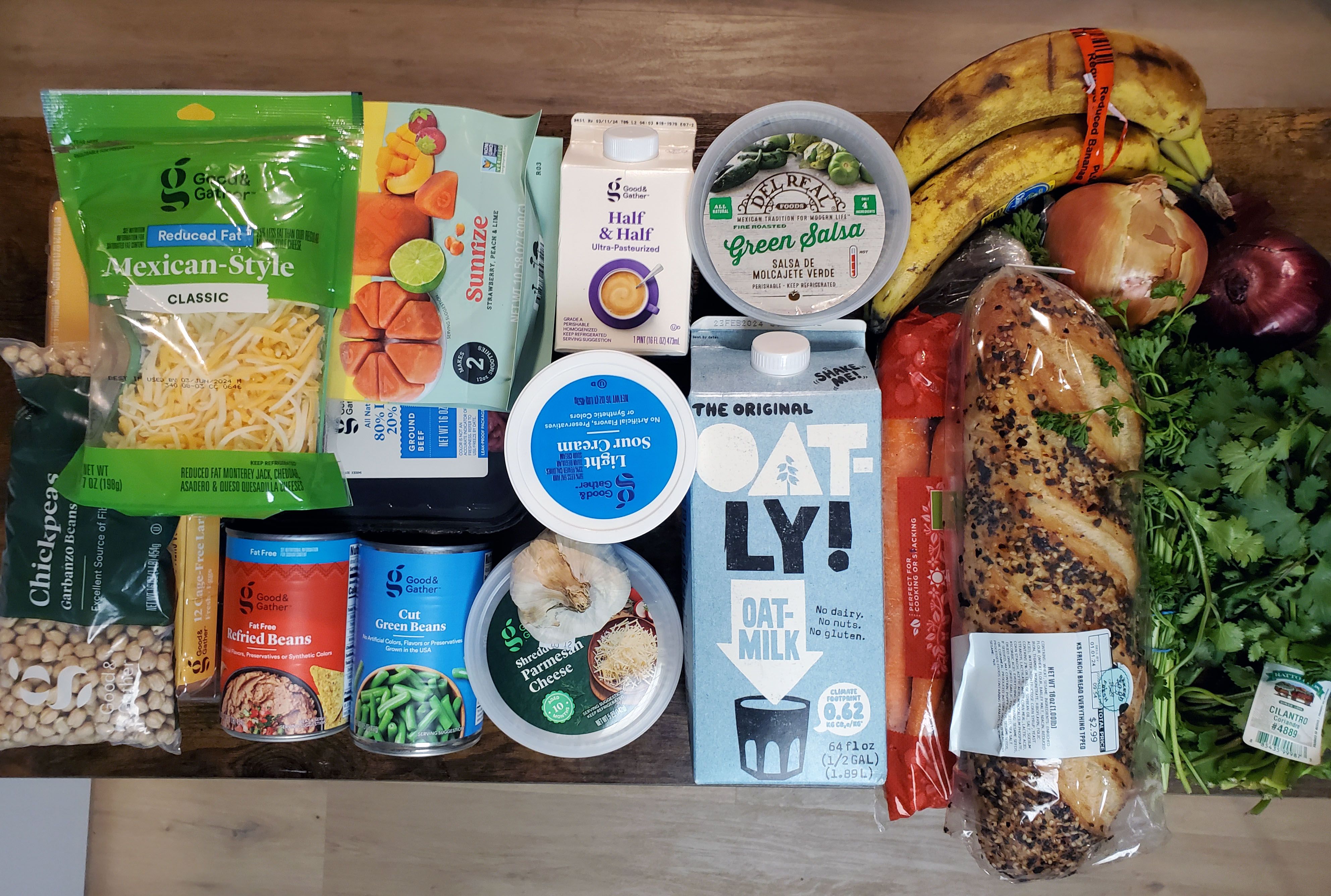 Groceries spead out on a table including oat milk, a loaf of bread, cans, cheese, and other items.