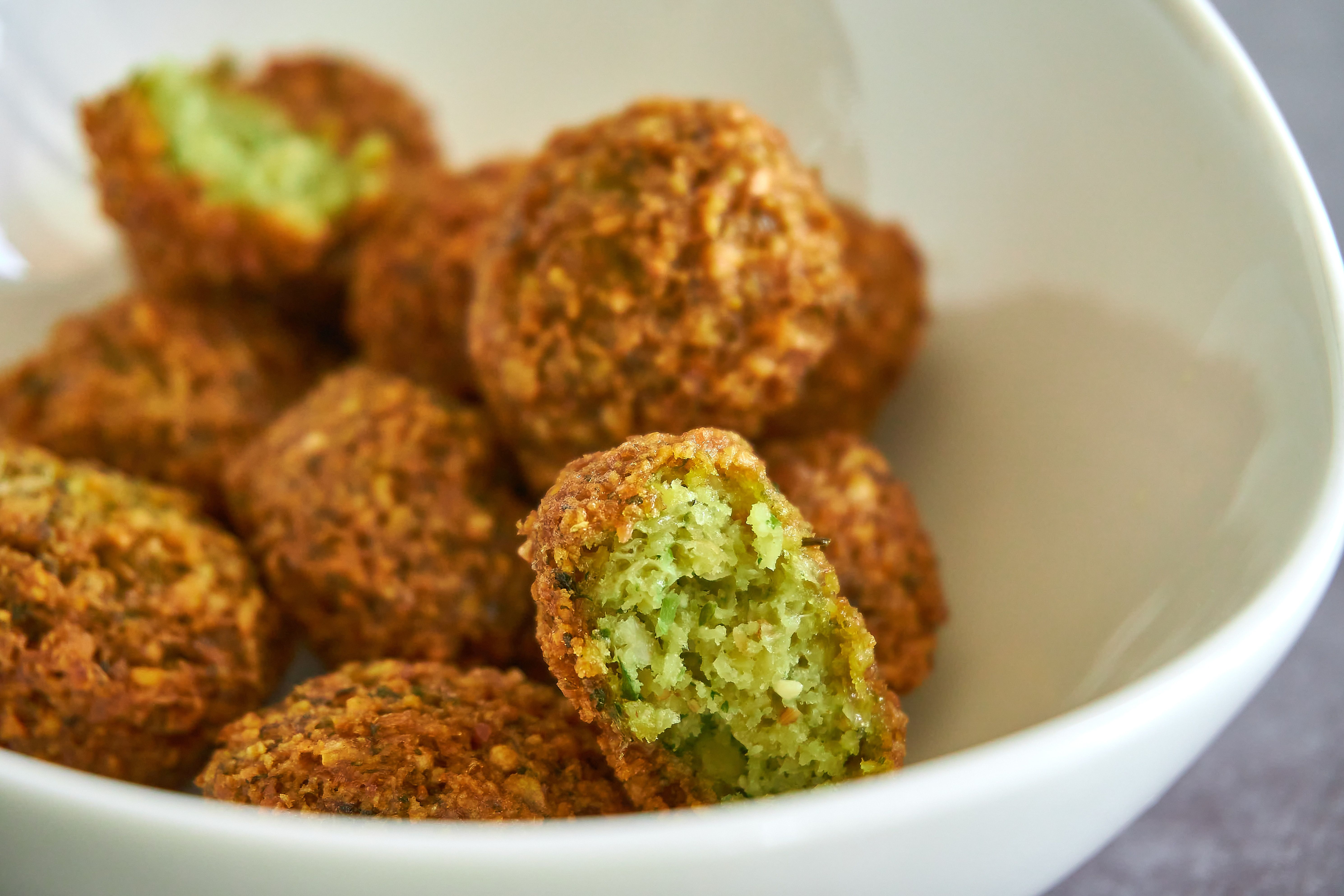 A bowl of falafel with one cut in half to see the green inside