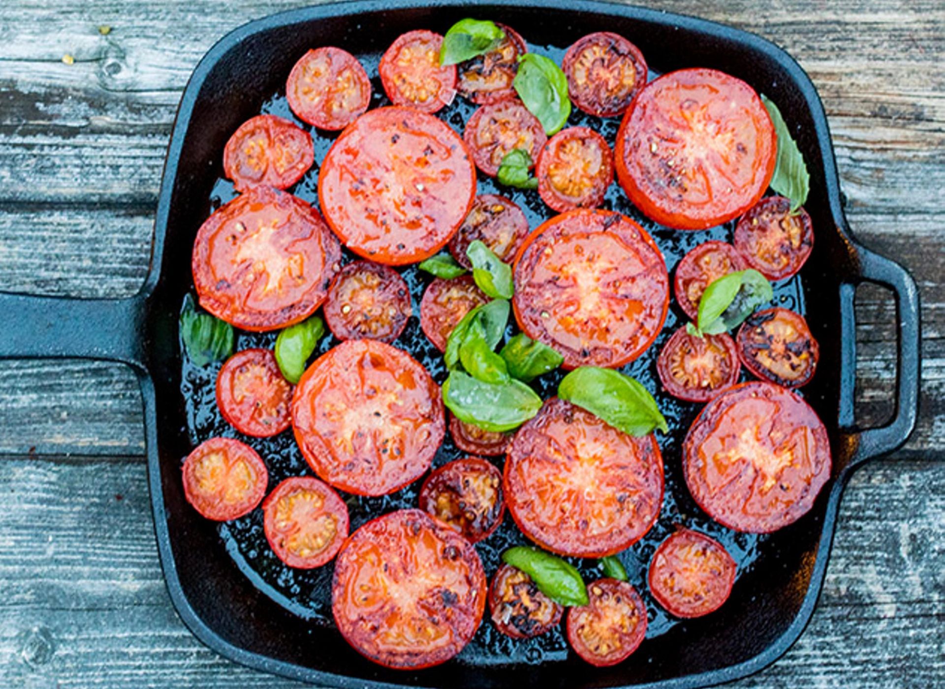 Stekte tomatskiver og cherrytomater i panne, toppet med friske basilikumblader.