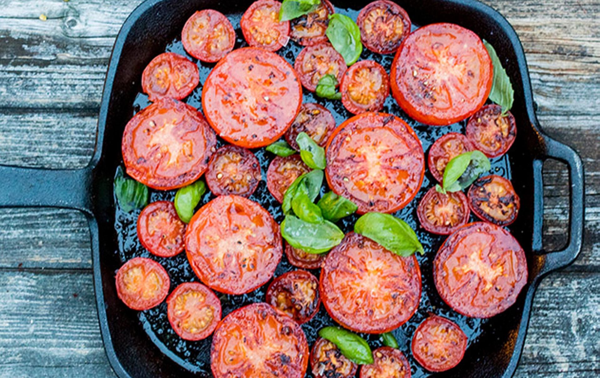 Stekte tomatskiver og cherrytomater i panne, toppet med friske basilikumblader.