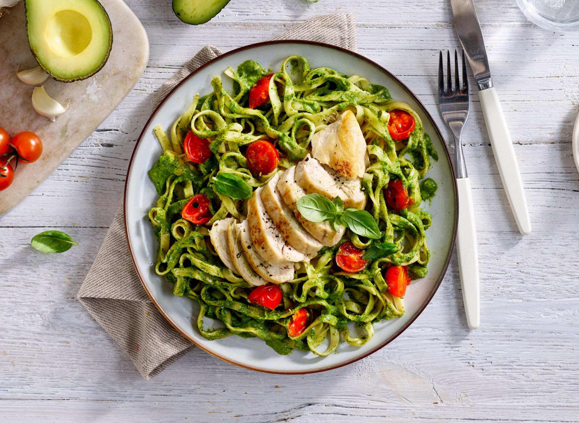 Kremet grønn pastasaus laget av avokado, spinat, basilikum og lime, servert med tagliatelle, cherrytomater og saftig skivet kyllingbryst. Dekorert med frisk basilikum på en lys tallerken. Sunn og enkel pastarett med avokado og kylling.