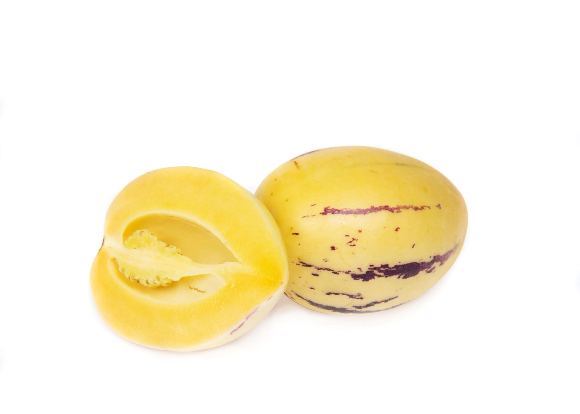 Pepinomelon (pepino dulce), én hel og én delt i to, som viser lyst gult fruktkjøtt og frø, plassert på hvit bakgrunn.