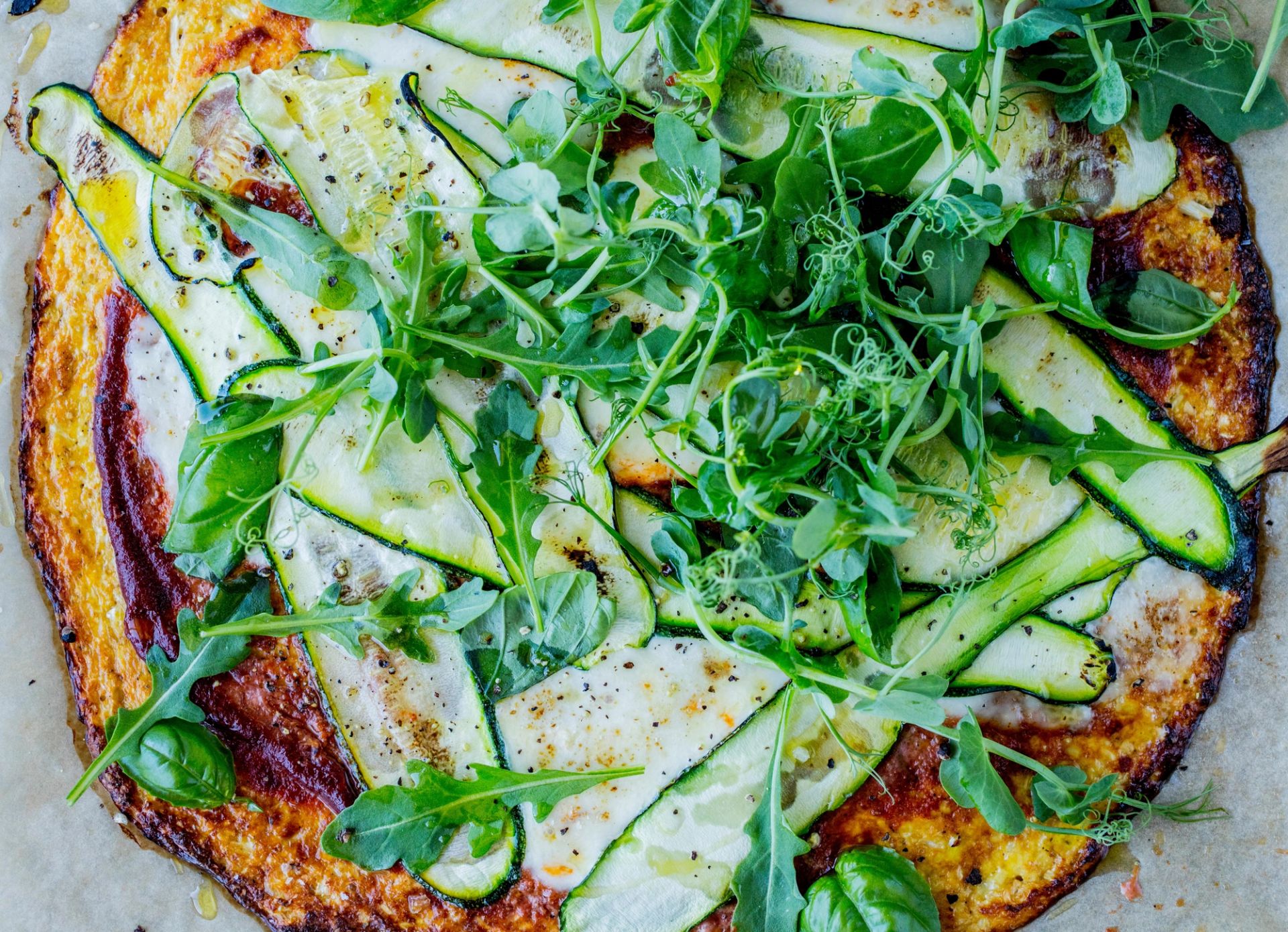 Vegetarpizza med tynne skiver squash, grønn salat og urter på en gyllen, rustikk bunn.