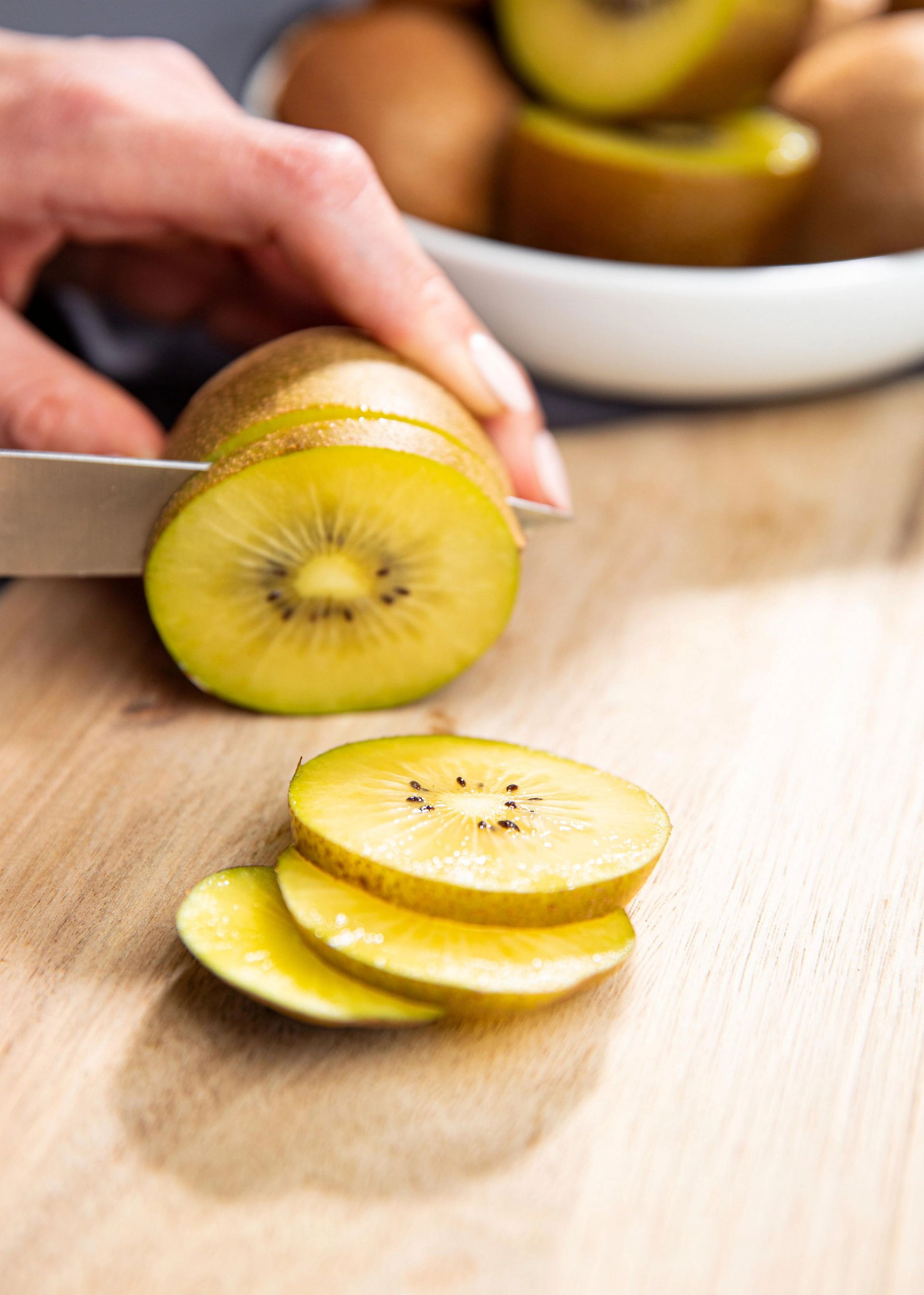 Kiwi som skjæres i skiver med kniv på et skjærebrett, med flere skiver lagt foran.