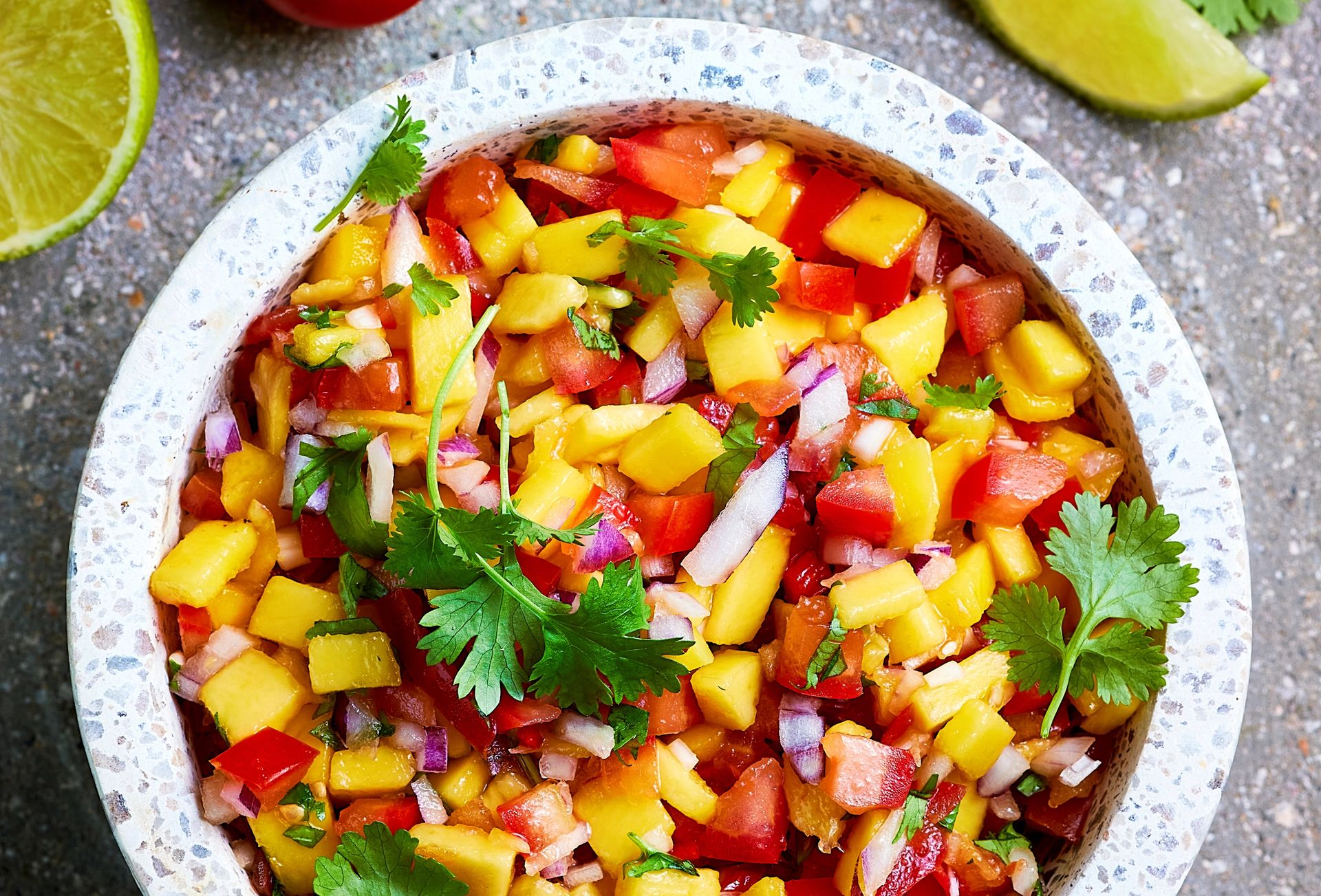Skål med fargerik mangosalsa laget av mango, tomat, rødløk, koriander og lime.