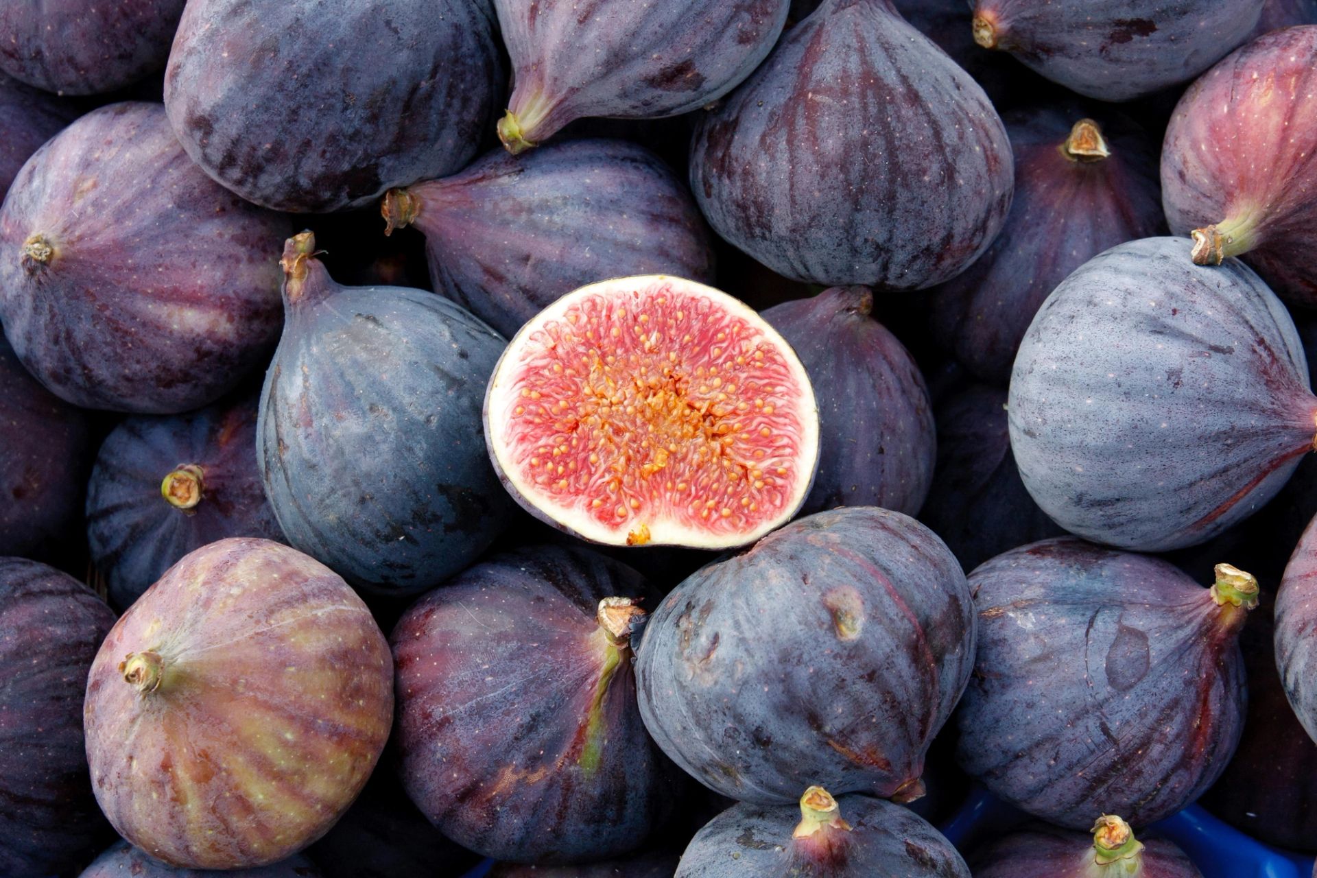 Nærbilde av ferske fikener med lilla skall, én fiken delt i to som viser rosa fruktkjøtt og frø.