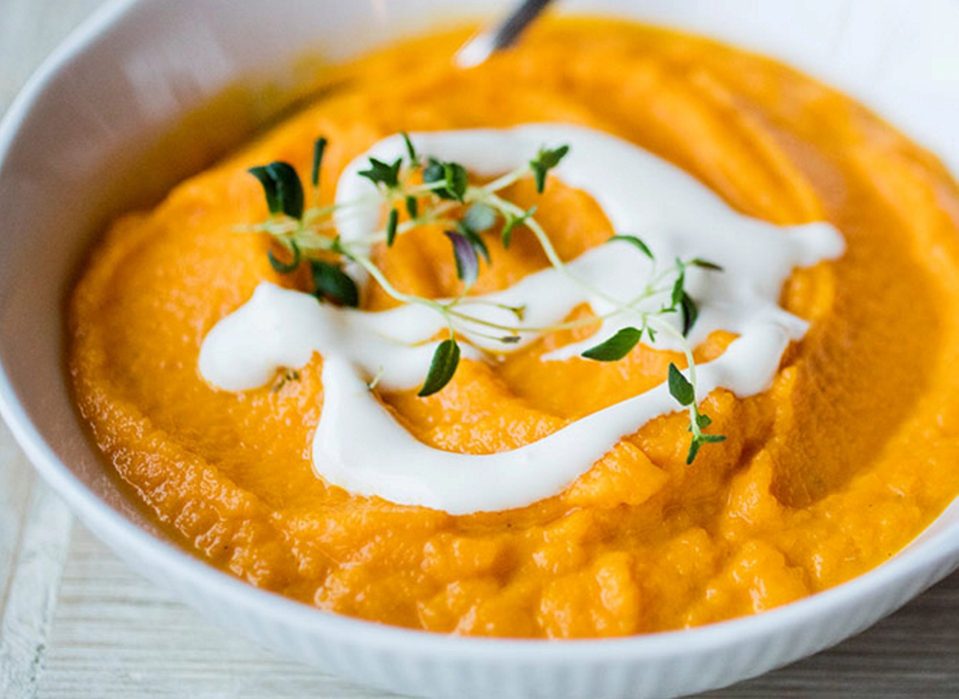 Kremete gulrotpuré i hvit skål, toppet med yoghurt og frisk timian.