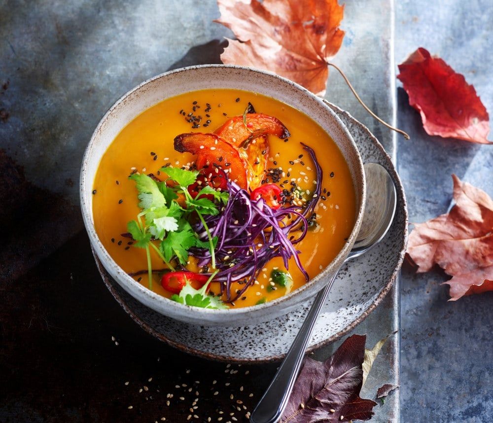 Thai-inspirert bakt gresskarsuppe toppet med koriander, sesamfrø og sprø grønnsaker, servert i keramisk bolle.