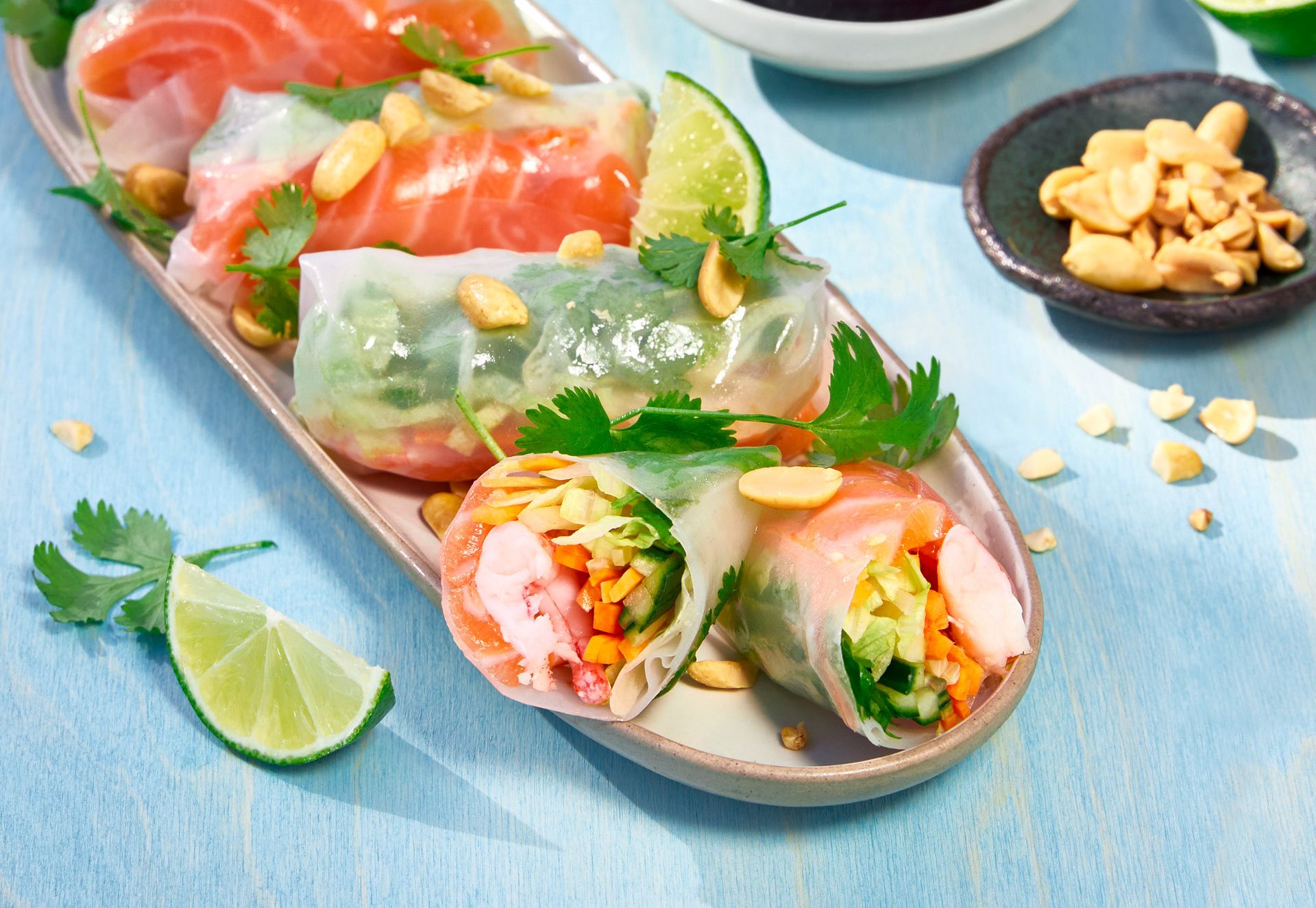 Friske vietnamesiske sommerruller med laks, grønnsaker og koriander, servert på fat med limebåter og peanøtter ved siden av.