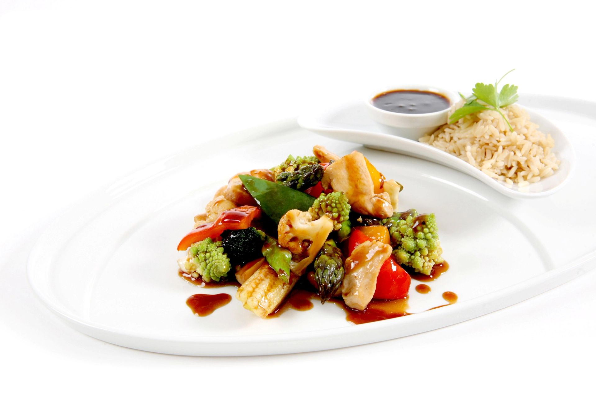 Stir‑fry med kylling og grønnsaker som brokkoli, romanesco, paprika og sukkererter i mørk saus, servert på hvit tallerken med ris og saus ved siden av