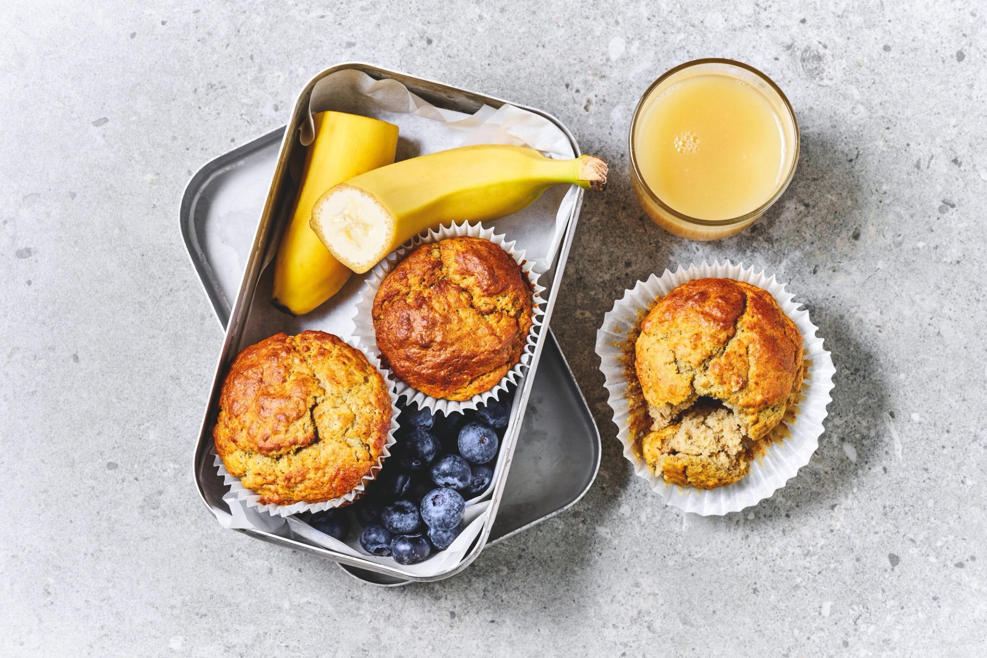 Grove muffins med bananskiver på toppen, ligende på et brett i lyngen. Rundt muffinsene ligger blåbær og jordbær.