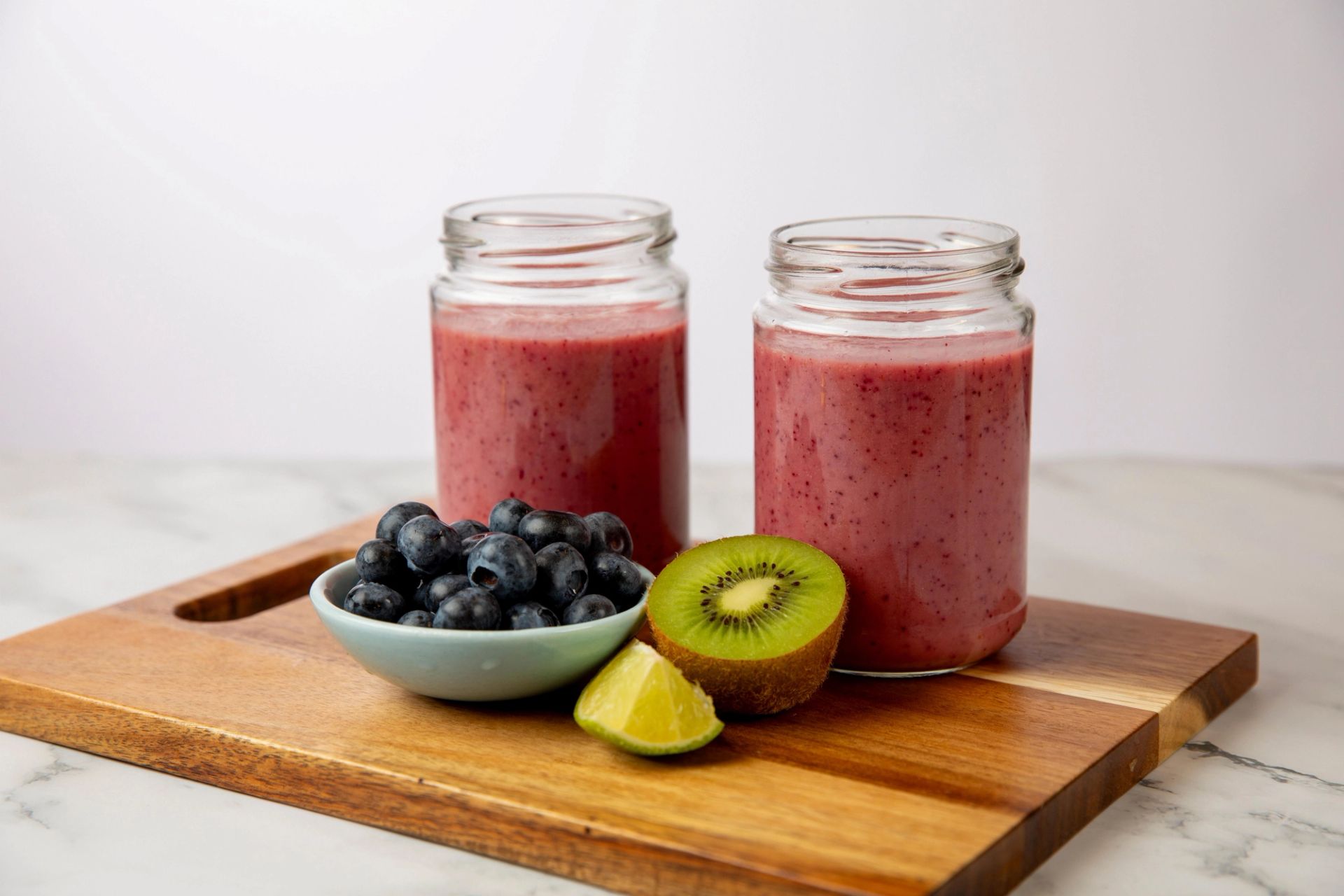 To glass med rosa smoothie, servert med blåbær, kiwi og lime på et trefat.