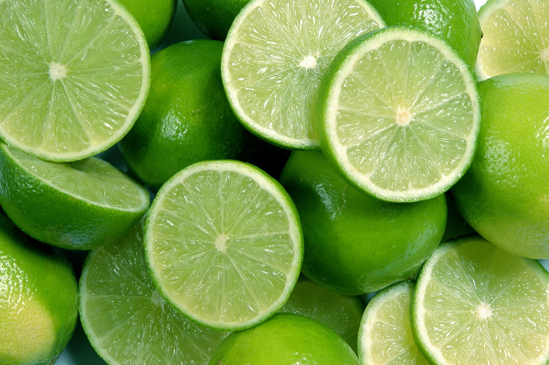 En haug med hele og oppskårne lime, der flere lime er delt i to og viser den lysegrønne, saftige fruktkjøttflaten.