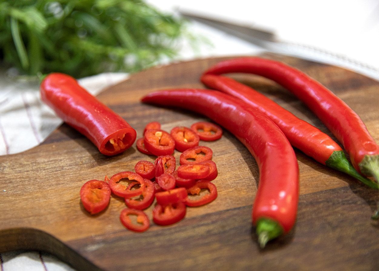 Røde chilipepper på et trebrett, hvor én er delvis oppskåret i tynne ringer som ligger spredt foran hele chilier.