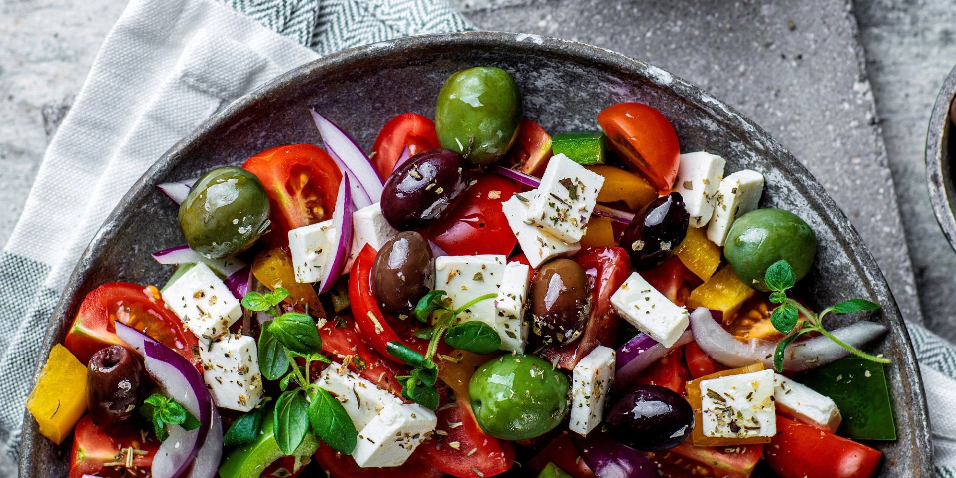 Gresk salat med fetaost, tomater, agurk, rødløk, paprika og oliven servert i en dyp tallerken.