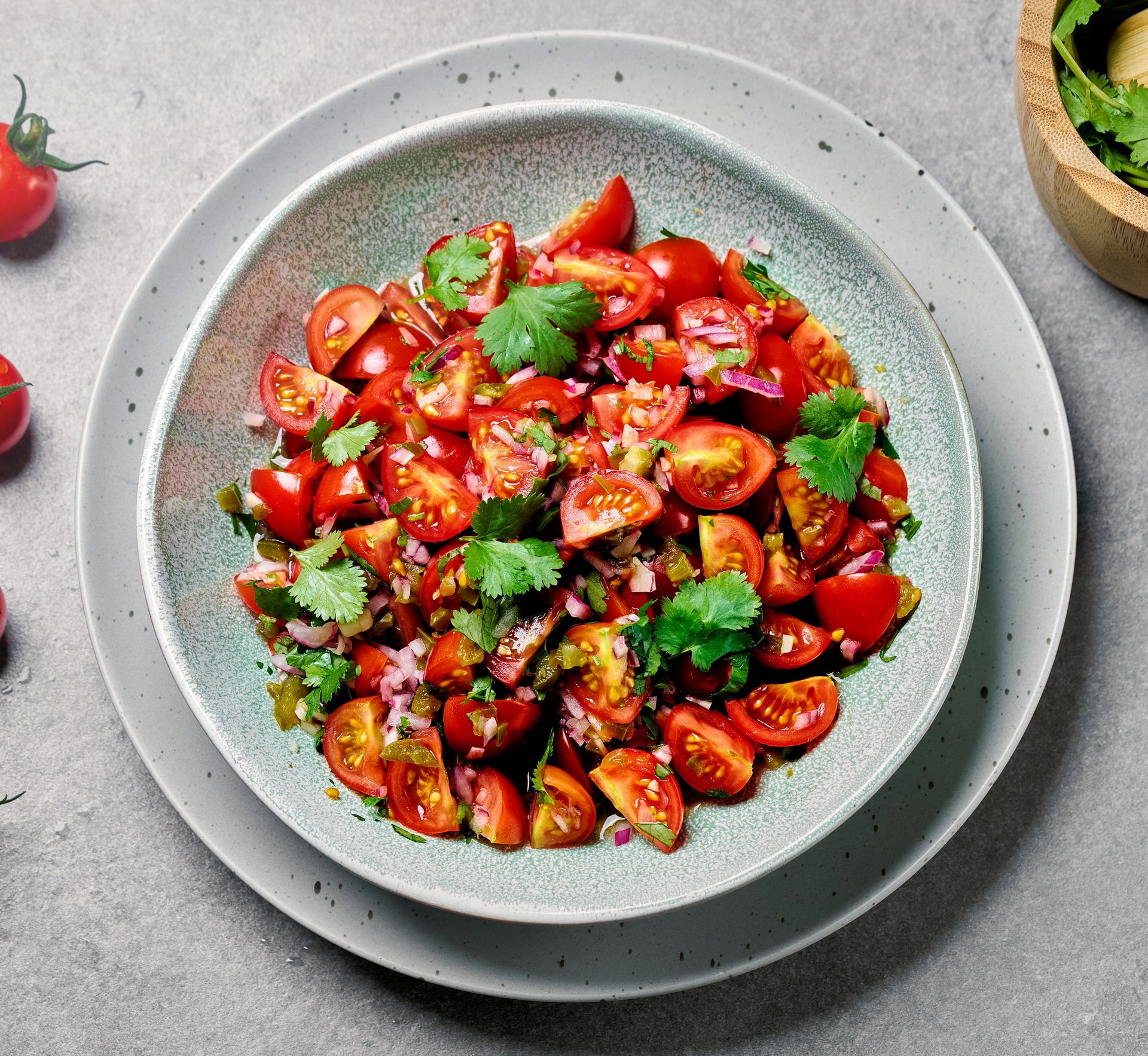 En tomatsalat i en grå skål med korianderblader på toppen på en grå bakgrunn. 