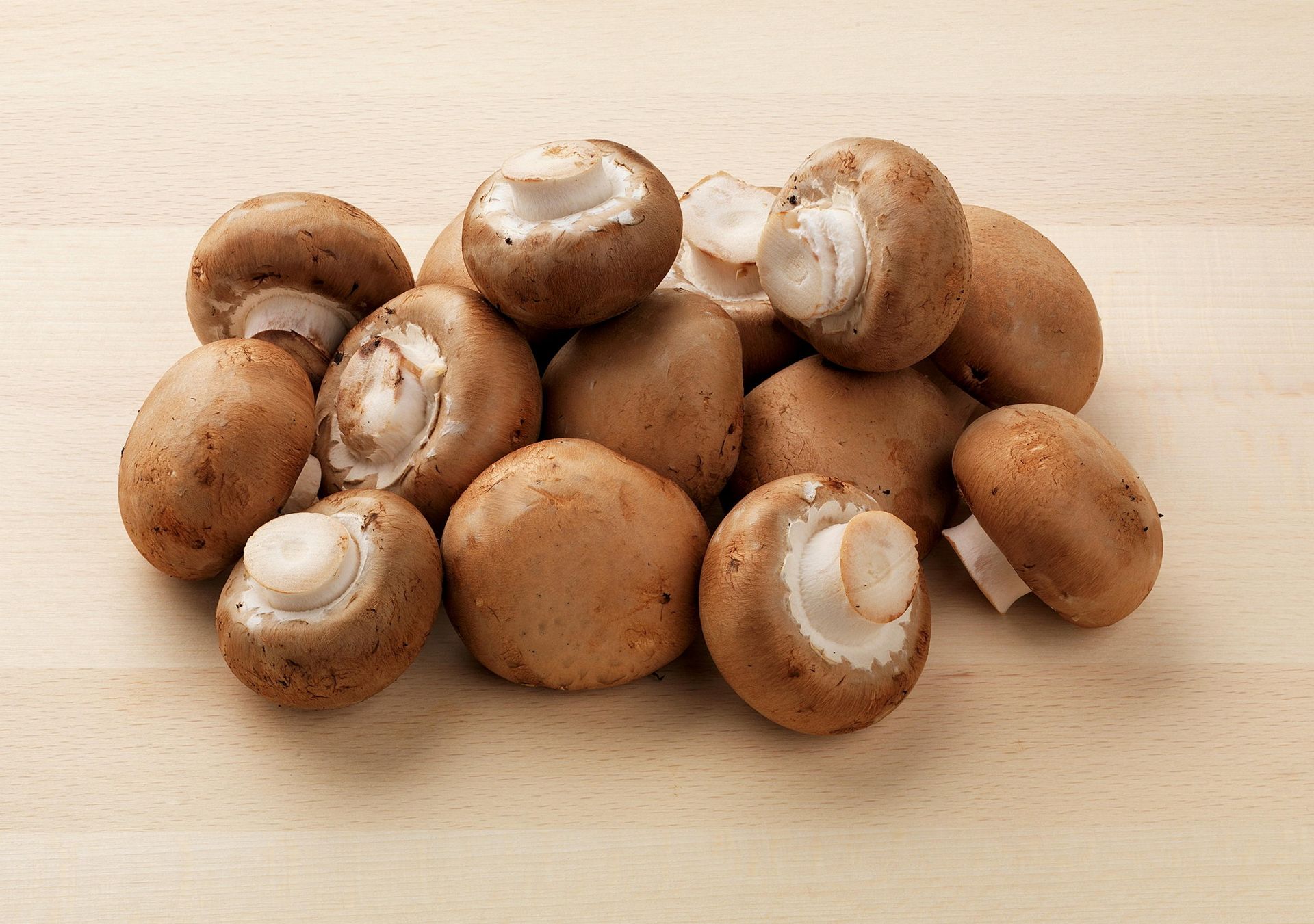 En haug med brune aromasopp lagt på en lys treflate. Soppene ligger tett samlet, med synlige hatter og korte stilker, og overflatene har en naturlig, litt ru tekstur.