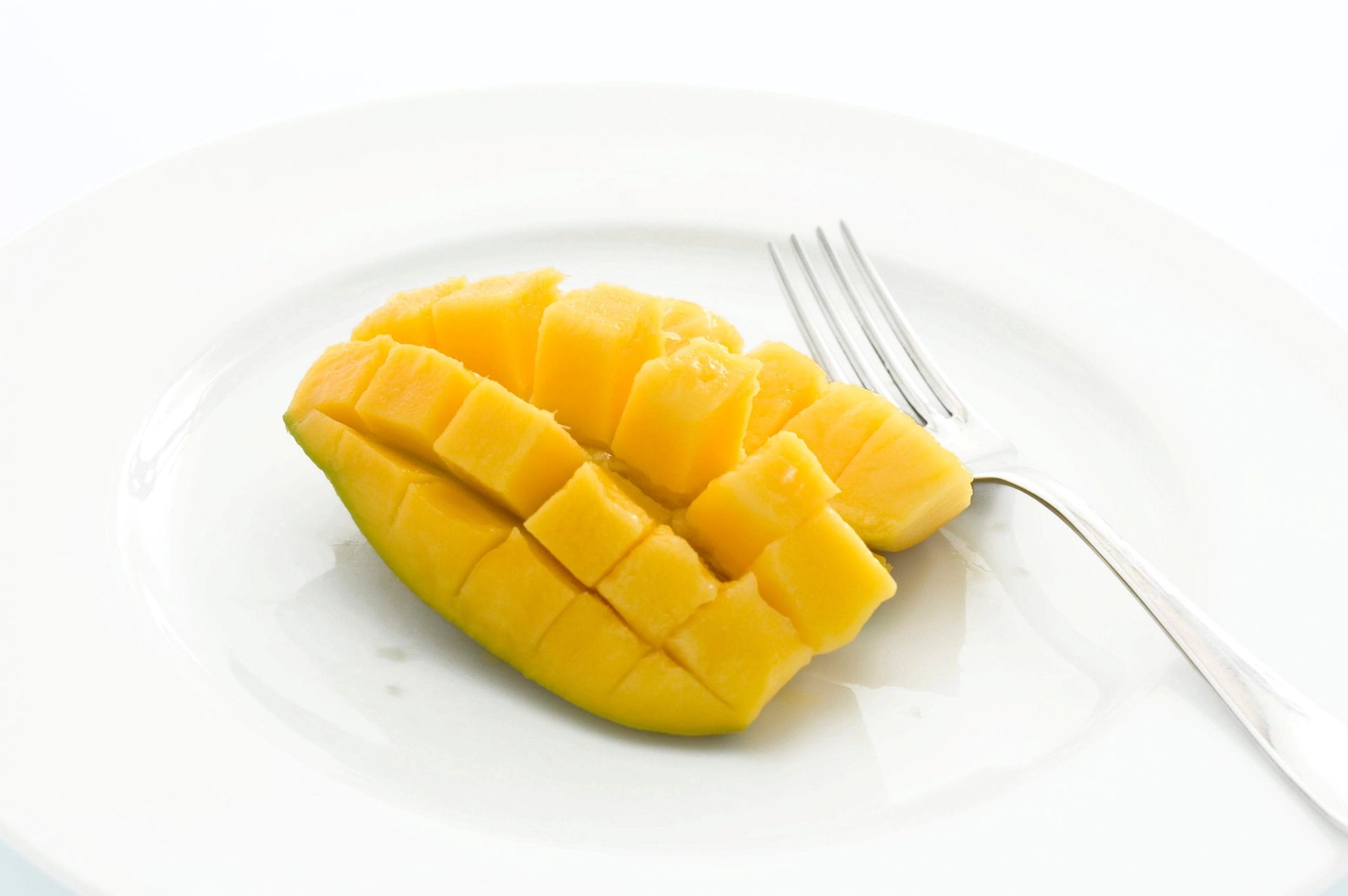 Oppskåret mango i rutenettmønster på hvit tallerken, med gaffel ved siden av.