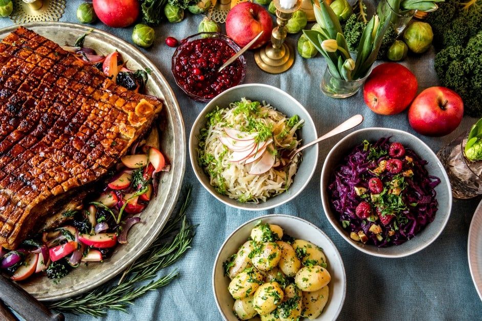 Ribbe med sprøstekt svor servert på et stort fat med epler og løk, omgitt av tradisjonelt norsk juletilbehør som poteter, rødkål, surkål og tyttebærsaus på et festdekket julebord.