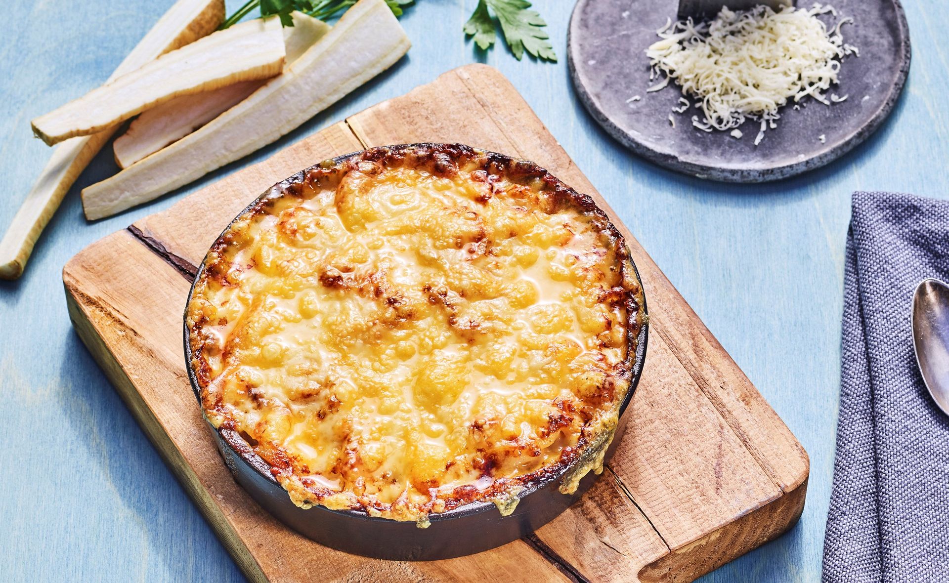 Grateng med persillerot og gyllen, gratinert ostetopping servert i en rund form på et trebord, omgitt av ferske persillerøtter og revet ost.