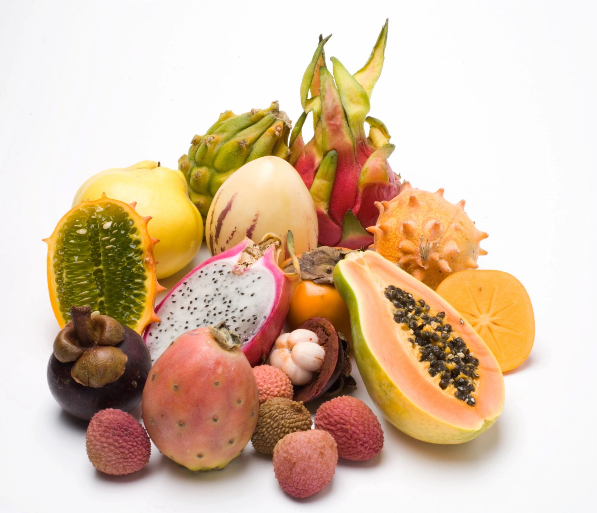 Et utvalg eksotiske frukter arrangert på hvit bakgrunn, inkludert papaya delt i to med frø, dragefrukt, litchi, mangostan, kaktusfiken, stjernefrukt, og hornmelon, vist både hele og oppskåret for å vise farger og teksturer.