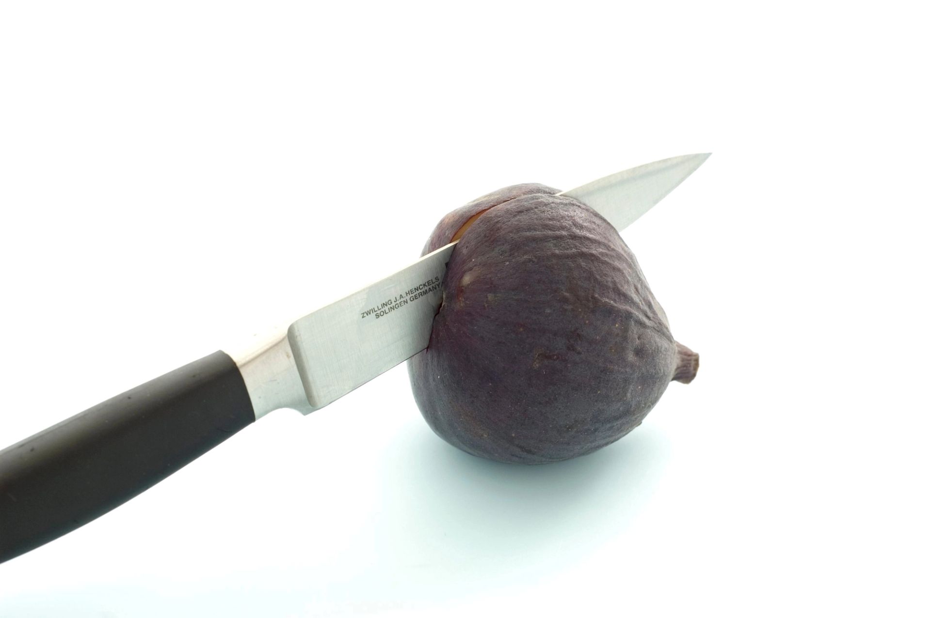 Fersk fiken som skjæres med kniv, plassert på hvit bakgrunn.