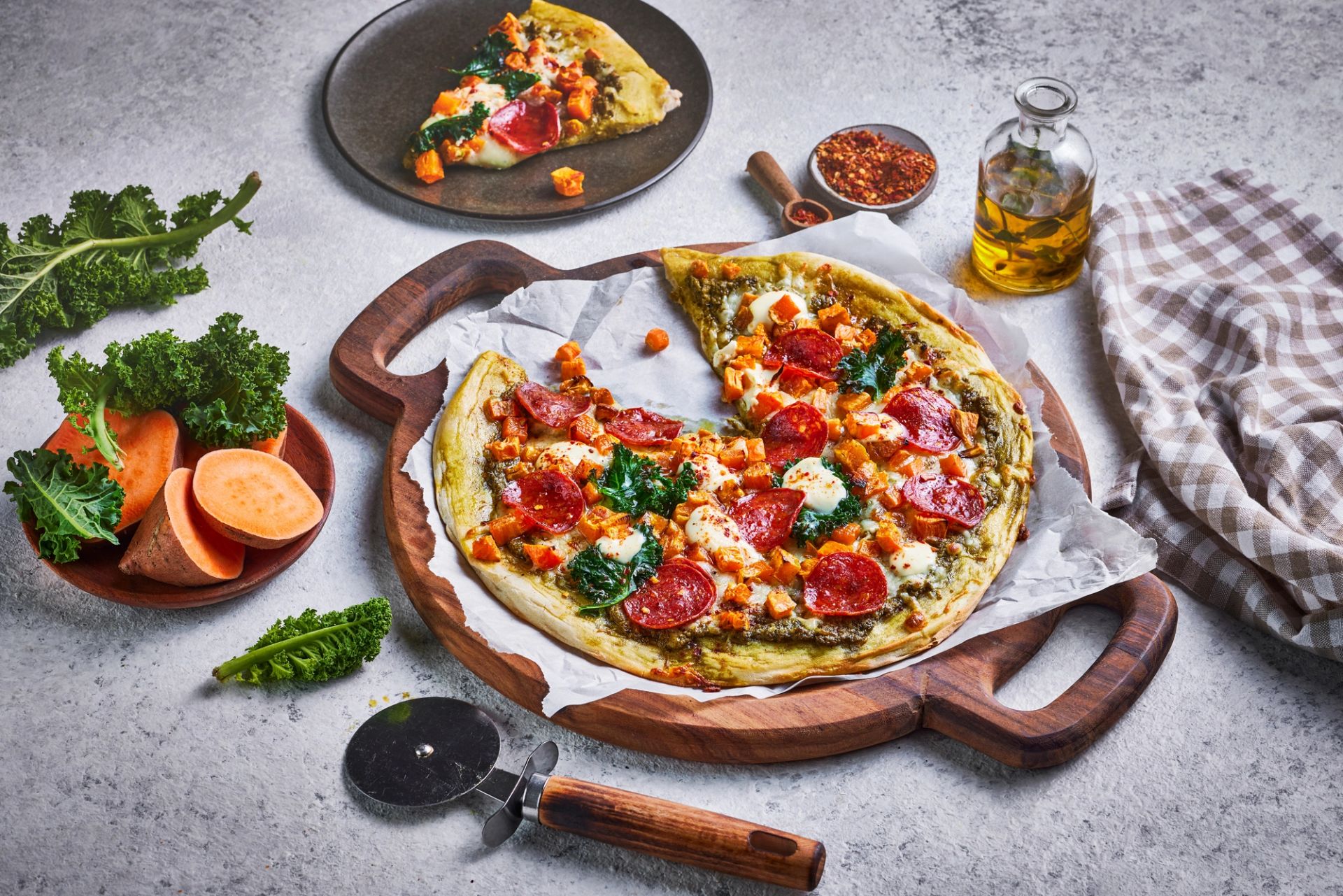 En hjemmelaget pizza med en pesto og ricotta, toppet med terninger av søtpotet, mozzarella og chorizo, servert på et rundt trefat med håndtak.