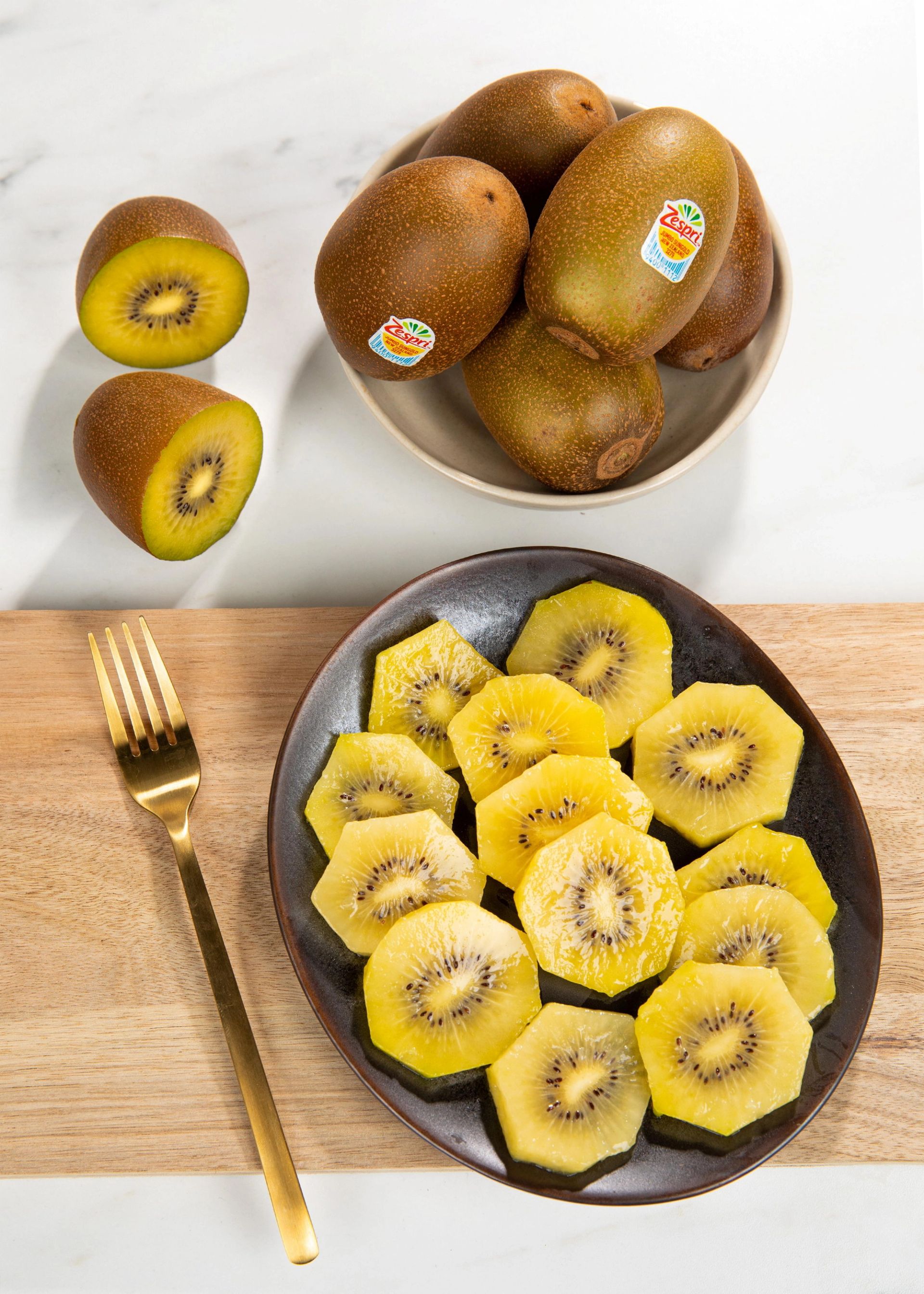 Gule kiwi, både hele og oppskårne, lagt på fat sammen med en gullfarget gaffel