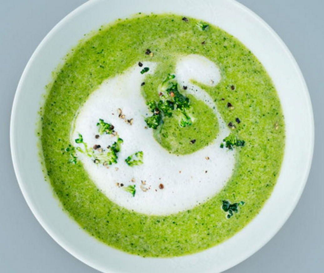 Skål med grønn, kremet brokkolisuppe toppet med en hvit krem­spiral, små grønne biter og et dryss pepper.