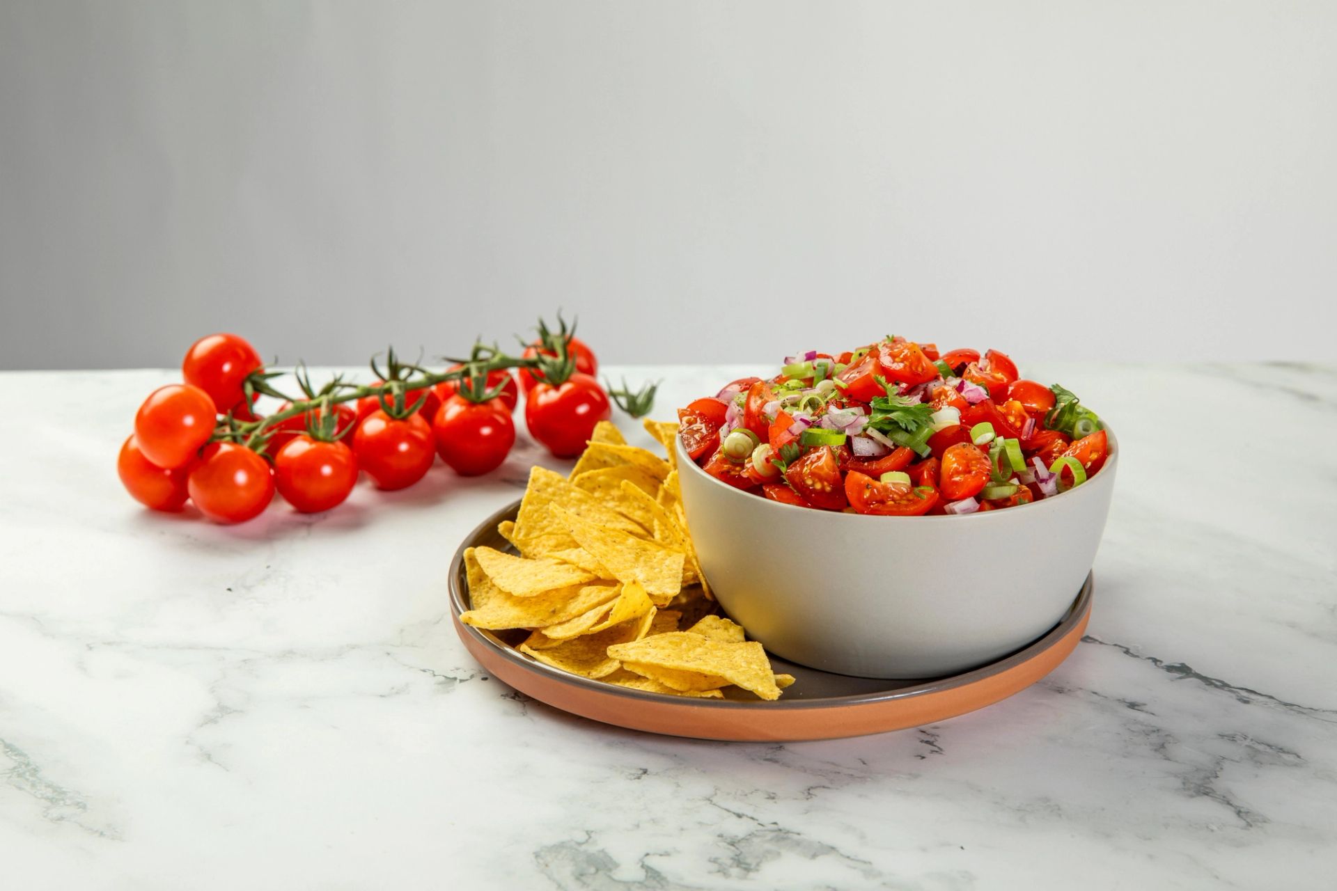 Skål med frisk tomatsalsa, servert med tortillachips på et fat, med tomater i bakgrunnen.