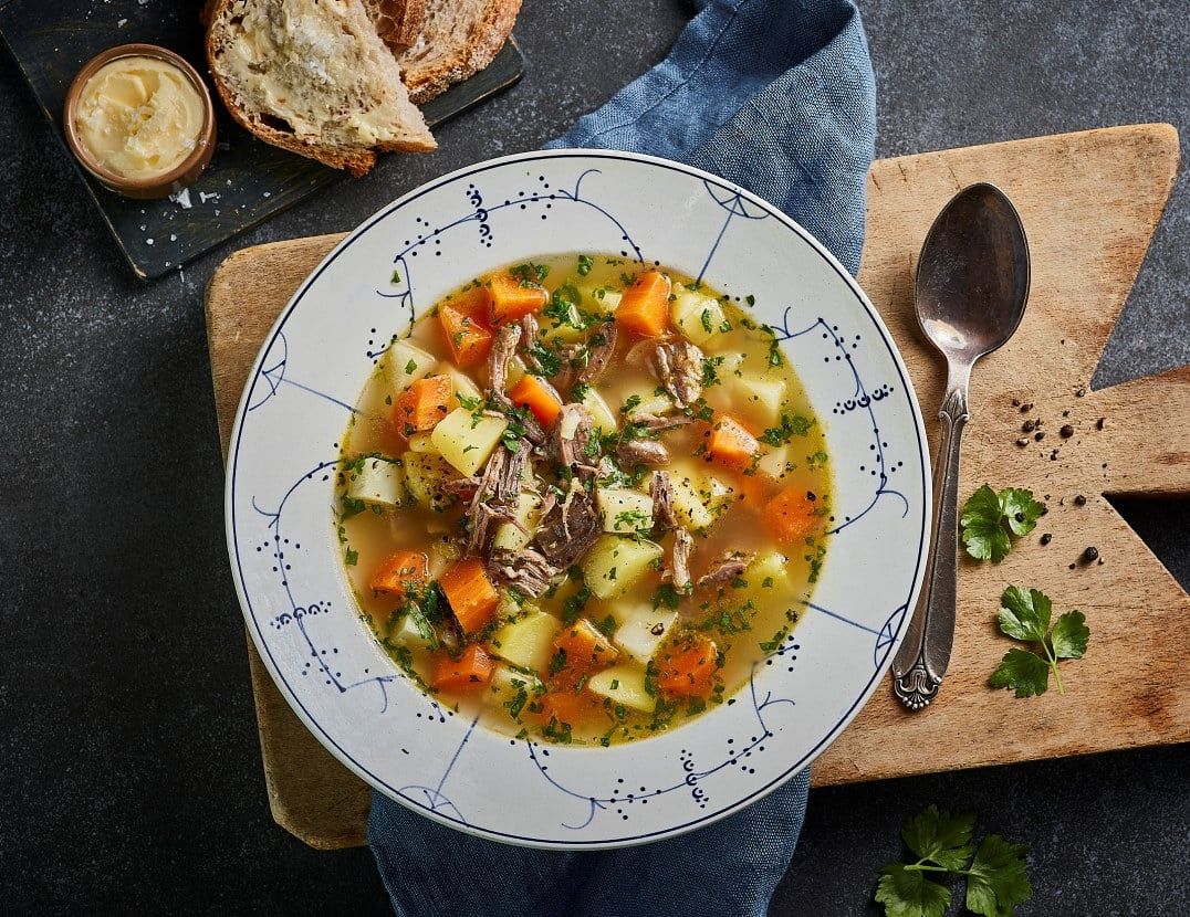 Grønnsakssuppe med pinnekjøtt, poteter og gulrøtter, servert i dyp tallerken med persille.