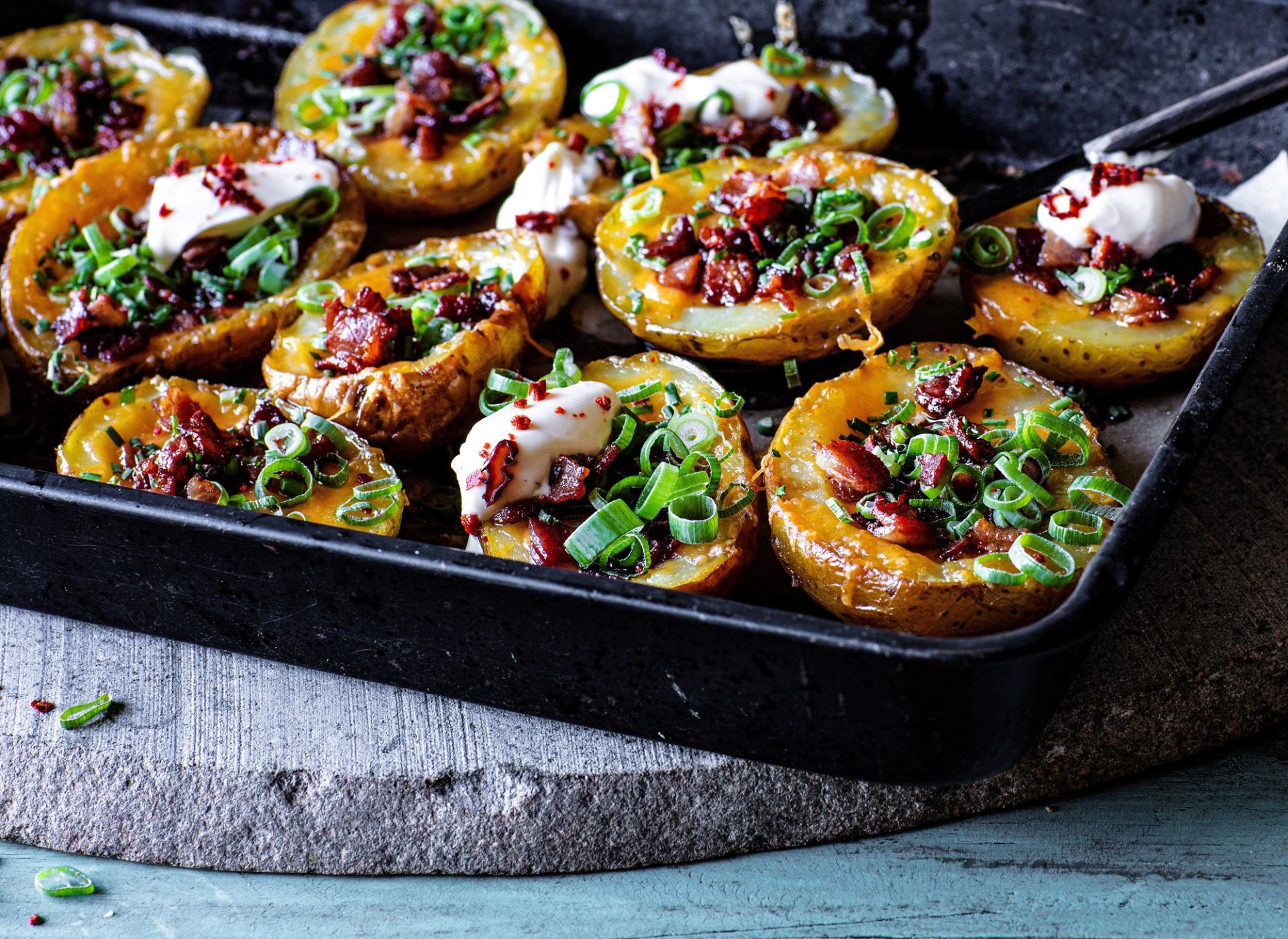Halverte, ovnsbakte poteter servert som "potato skins" i en sort metallform. Potetene er fylt med smeltet ost, sprøstekt bacon og rikelig med frisk vårløk. Noen av potetene er toppet med en klatt rømme.