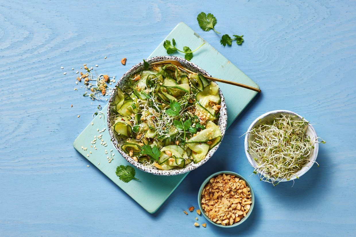 Asiatisk agurksalat med tynne agurkskiver, koriander, spirer og hakkede peanøtter i lett asiatisk dressing servert i skål.