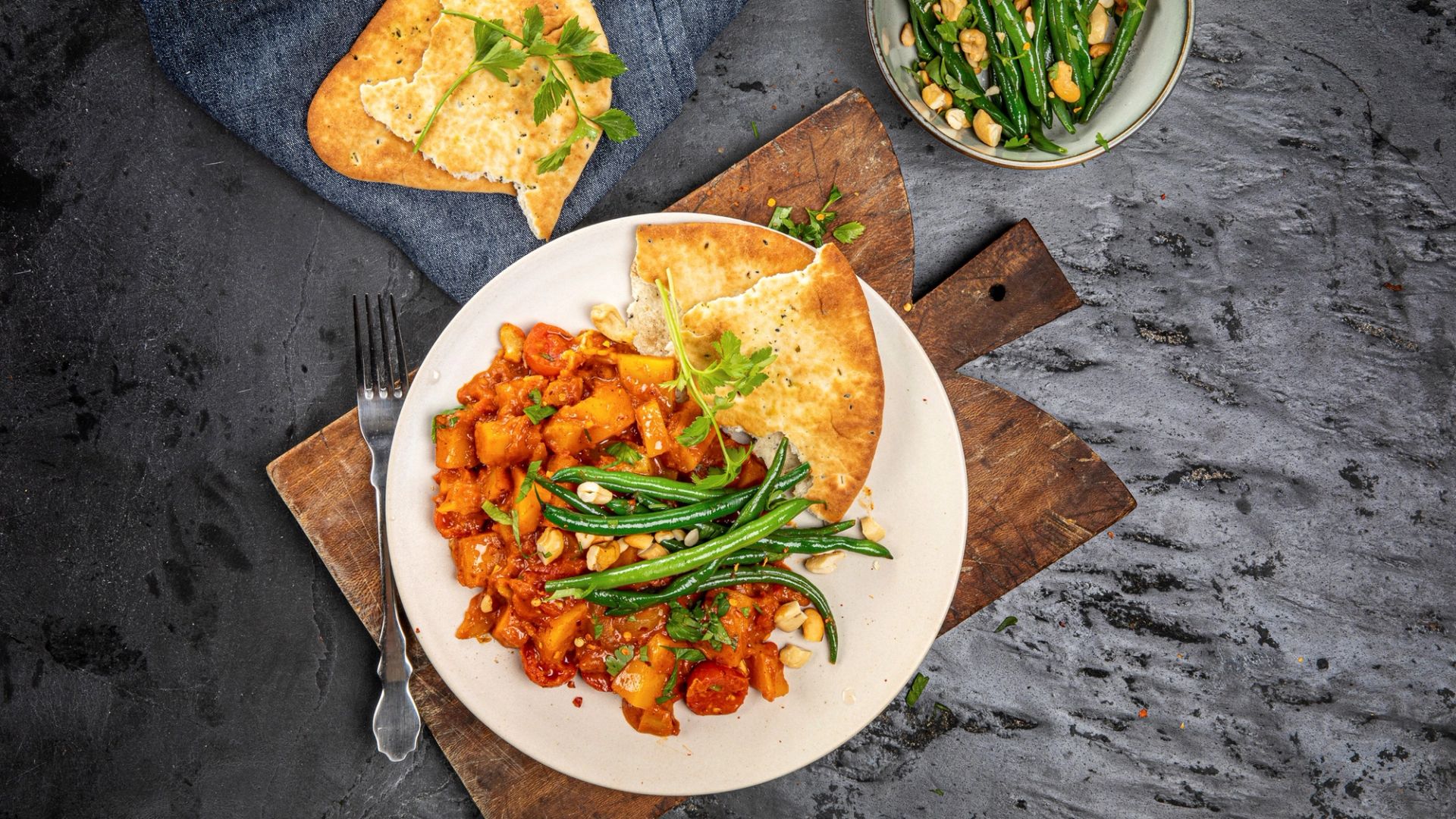 Tikka masala med gresskar, poteter og grønne bønner, servert med naan og friske urter.